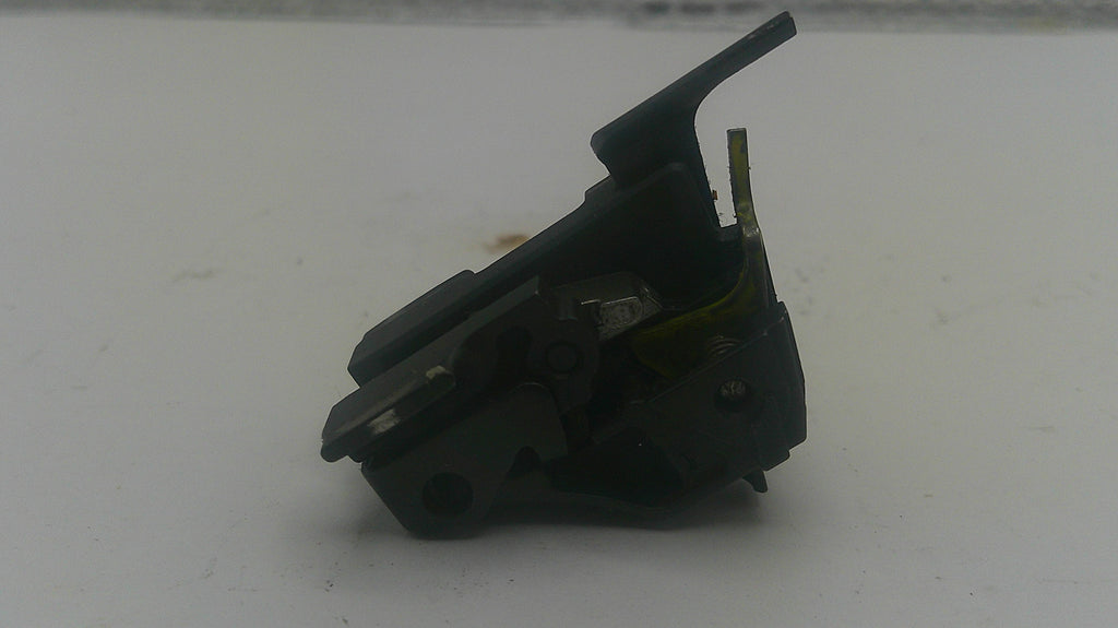 A small black plastic mechanical component or switch assembly with a hinged tab, photographed on a plain light gray surface.