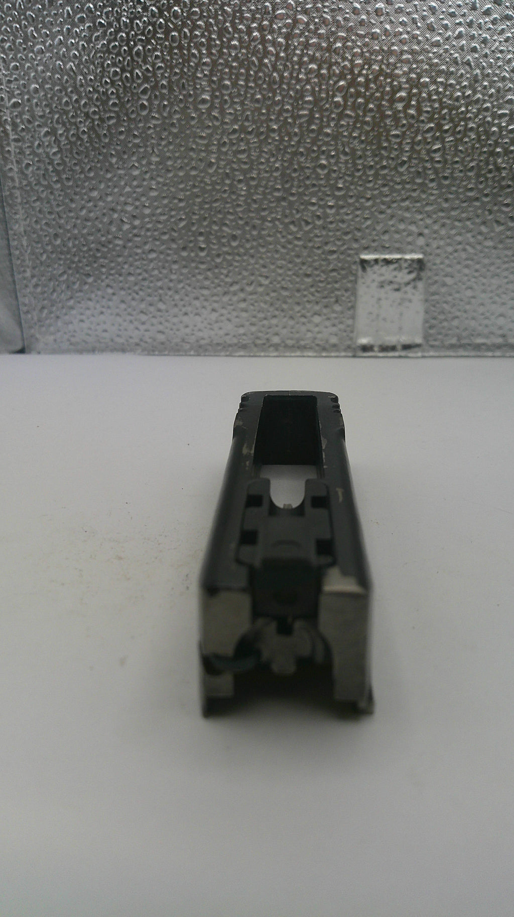 Black plastic component on a white surface with a textured gray background