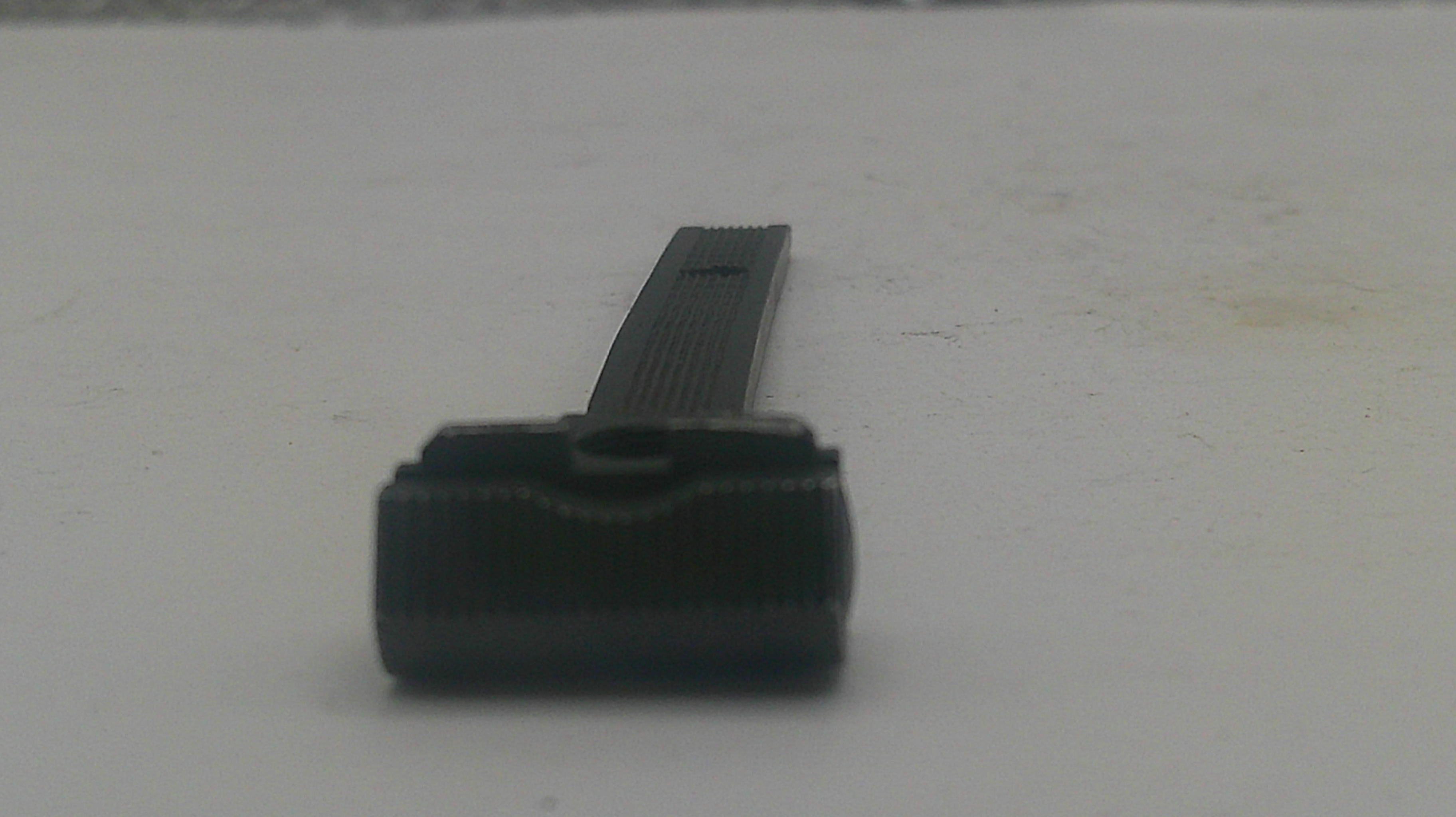 A small black plastic replacement part, possibly a cap or cover, shown on a plain light gray surface.