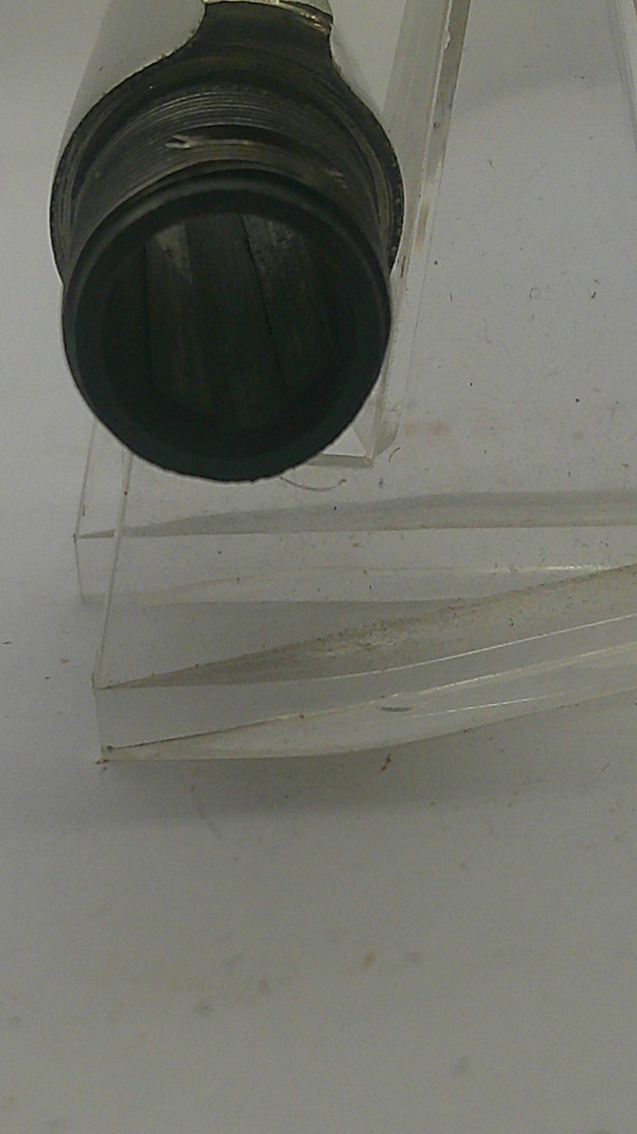 A close-up of a dark circular filter or mesh component attached to a clear plastic or acrylic frame against a plain off-white background.