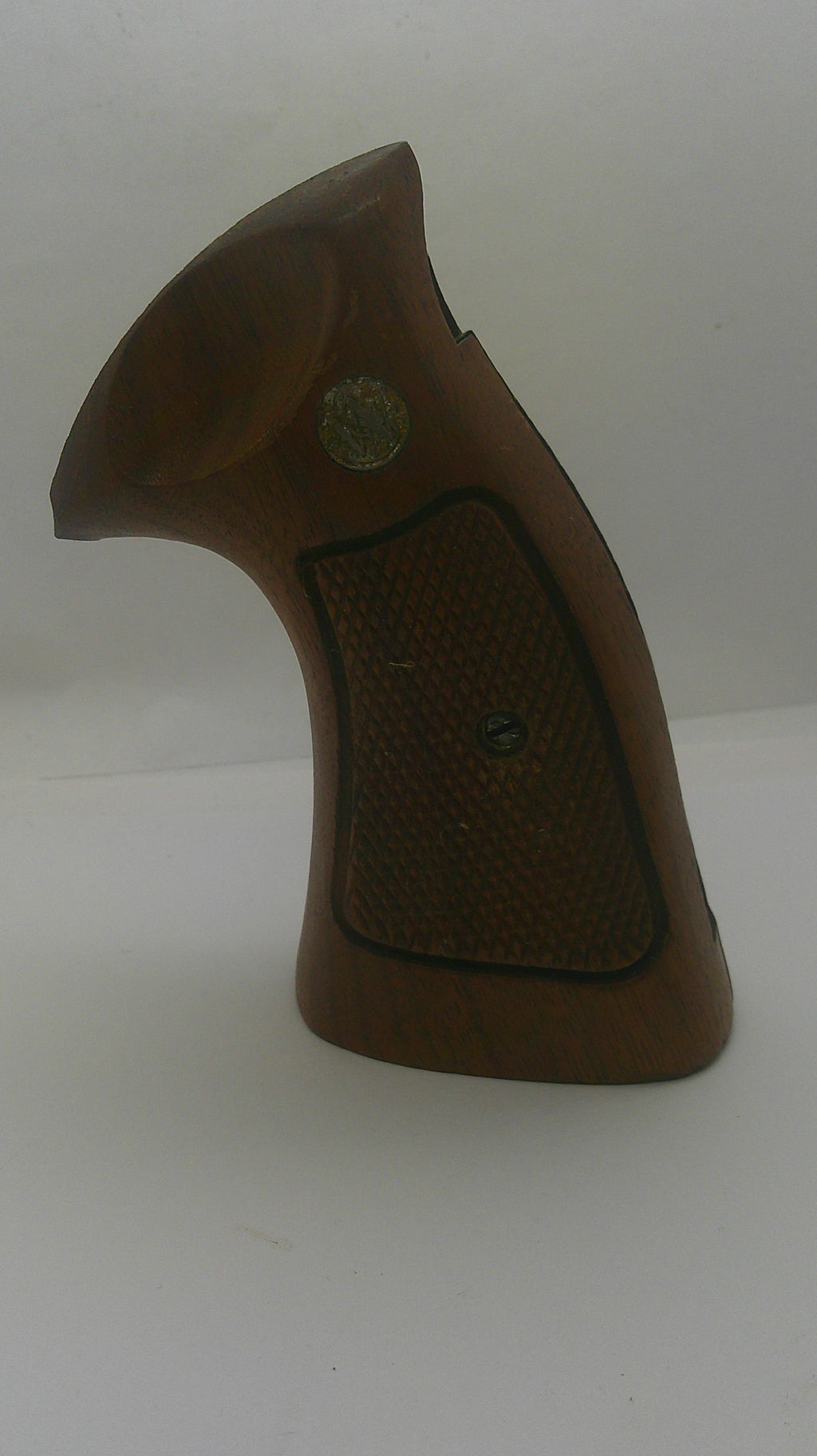 A brown wooden gun grip with a textured checkered pattern and a small brass emblem, shown against a plain off-white background.
