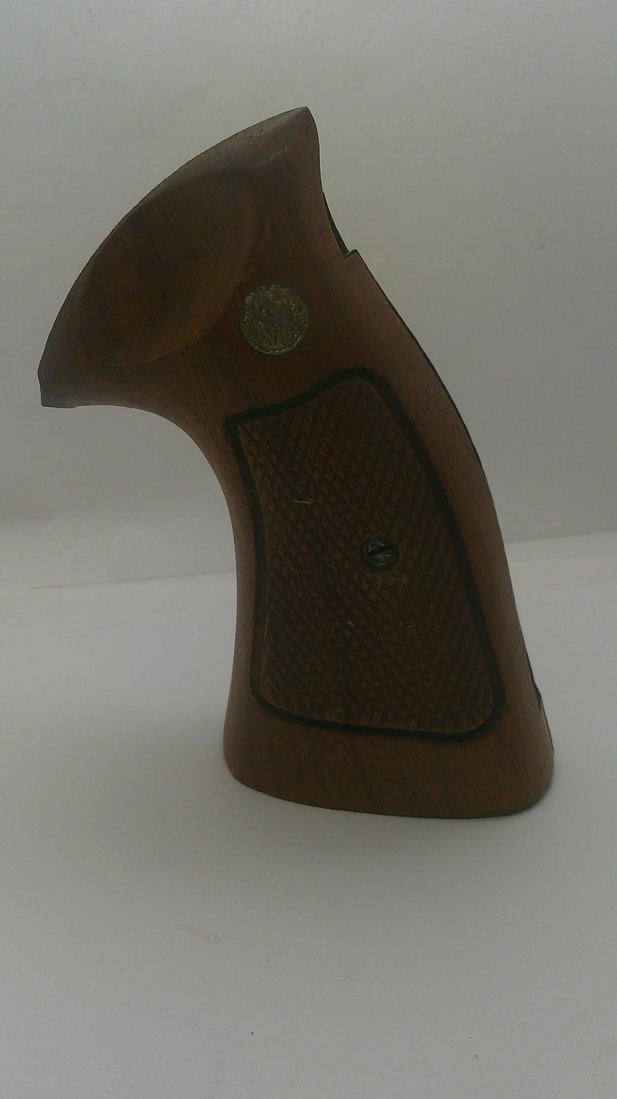 A brown wooden gun grip with a textured checkered pattern and a small brass emblem, shown against a plain off-white background.