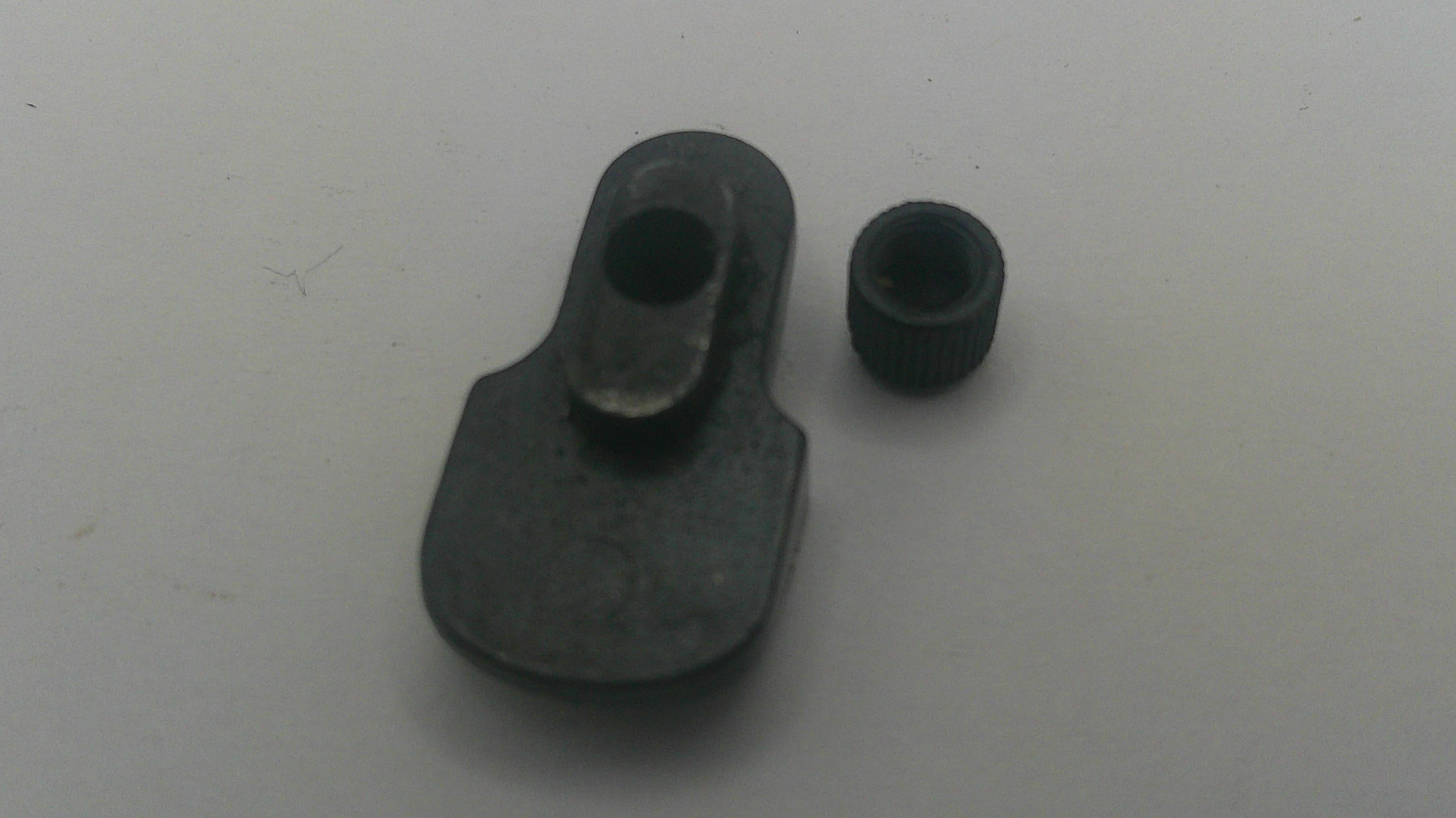 A pair of small black metal mechanical parts, including a larger flat piece with a circular opening and a smaller threaded cap, on a plain light gray background.