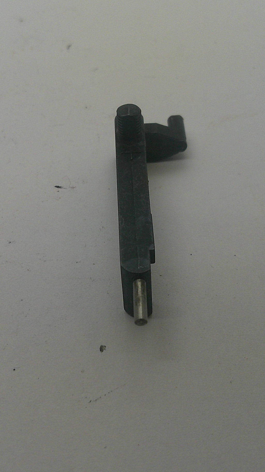 A small black plastic mechanical part with a silver metal pin, photographed on a plain off-white surface.