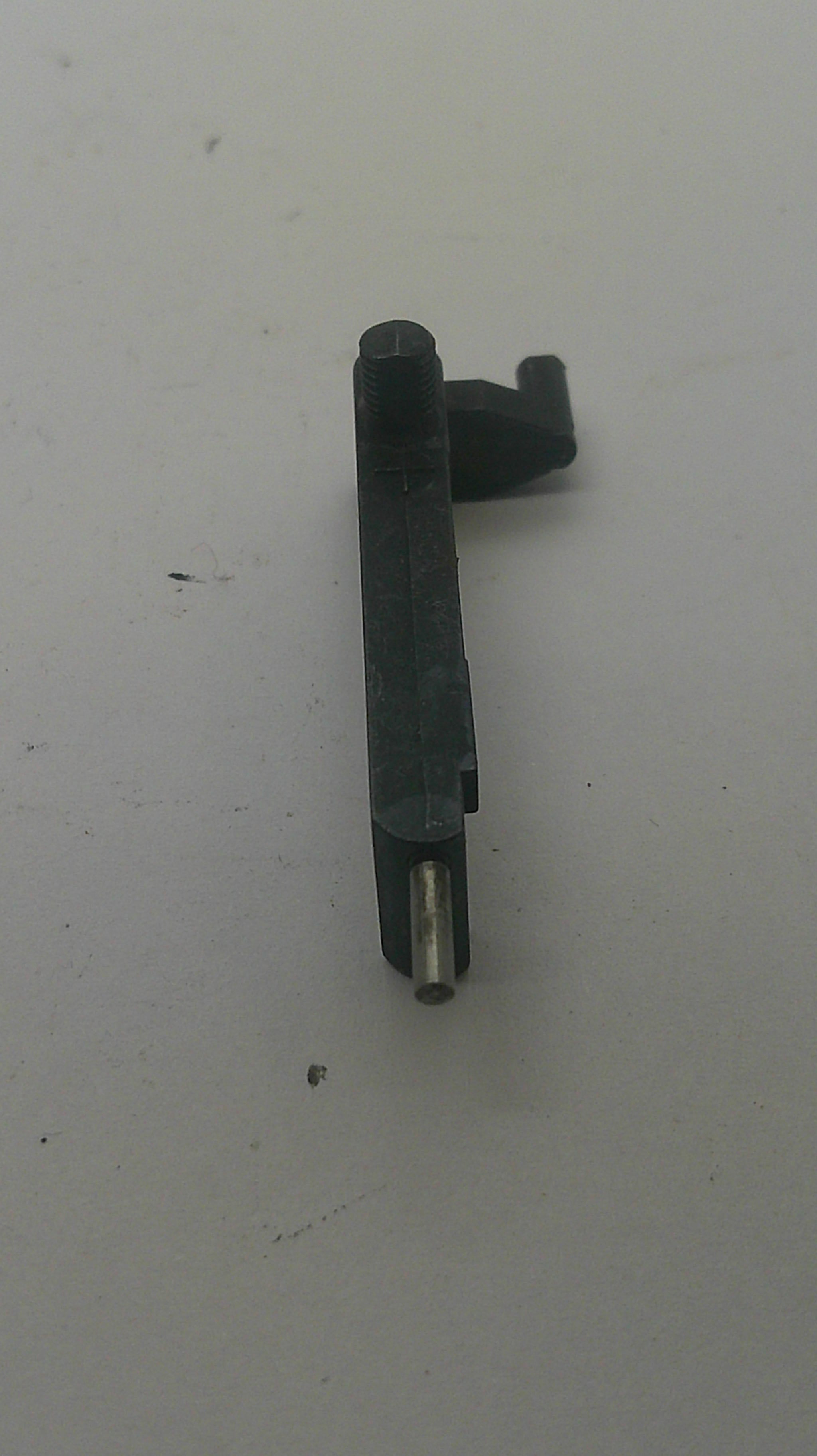 A small black plastic mechanical part with a silver metal pin, photographed on a plain off-white surface.
