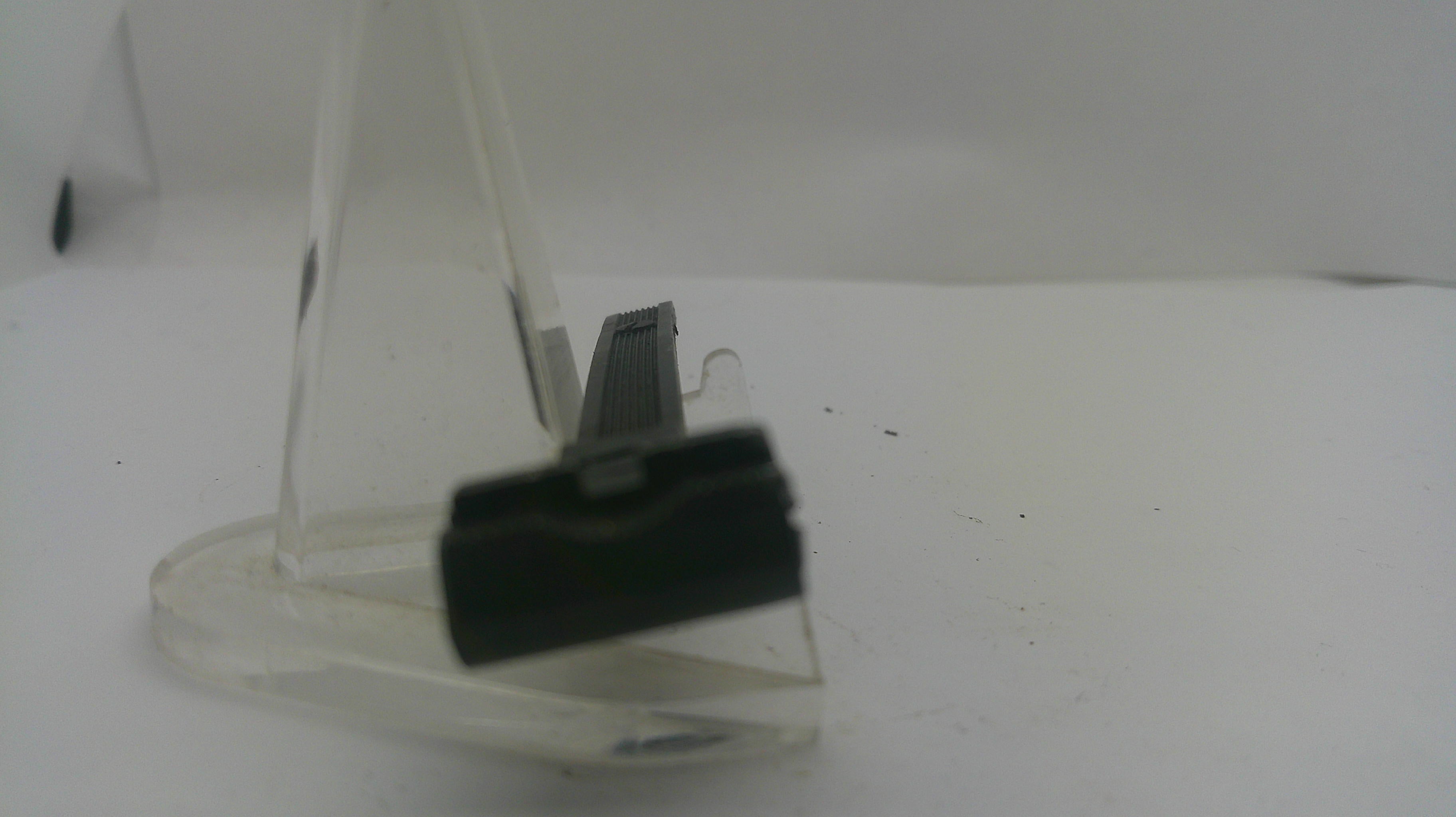 A close-up of a black plastic clip or connector mounted on a clear acrylic stand against a plain white background.