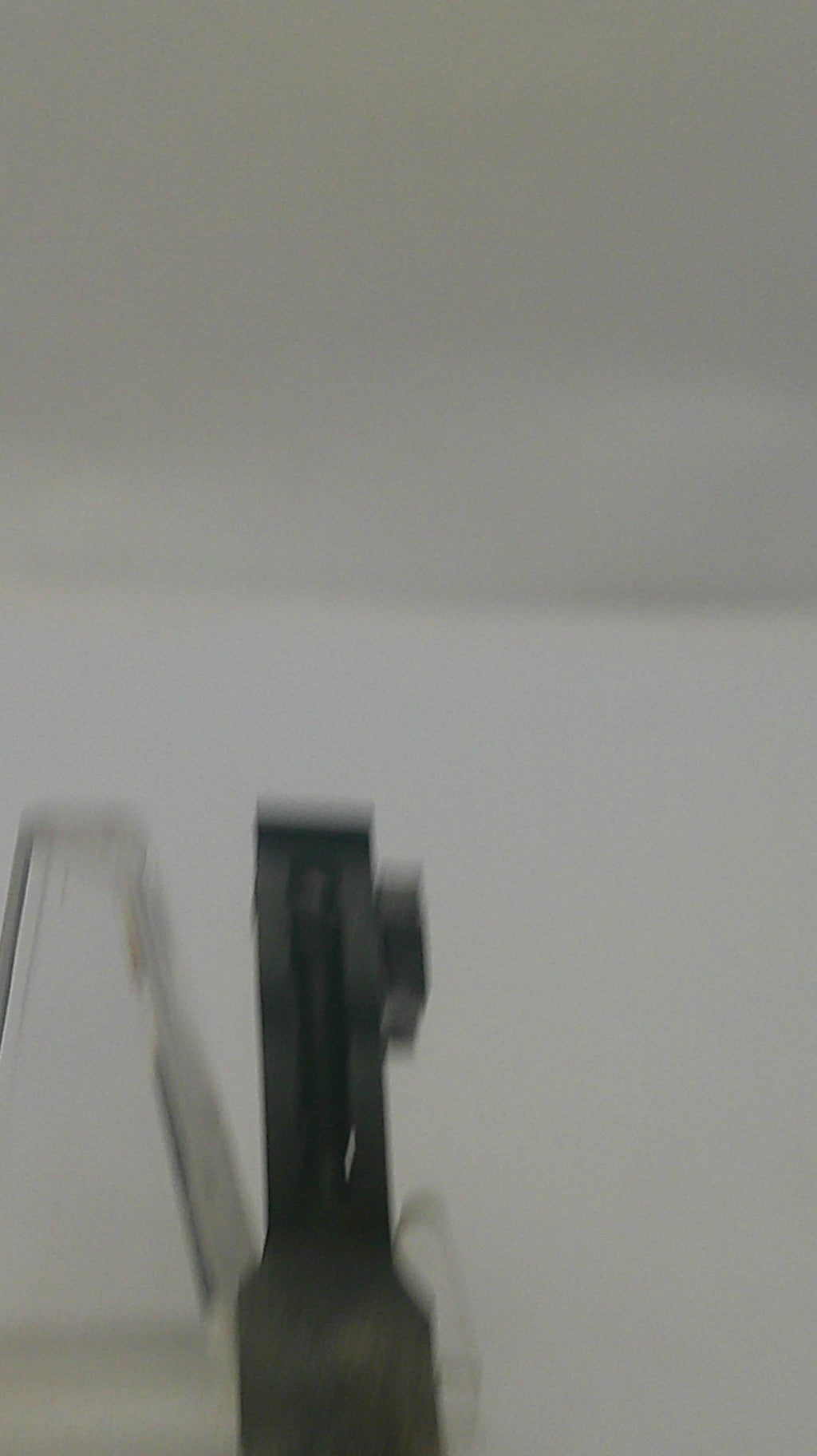 A close-up, slightly blurry shot of a black plastic mounting bracket or clip attached to a light gray or off-white wall.