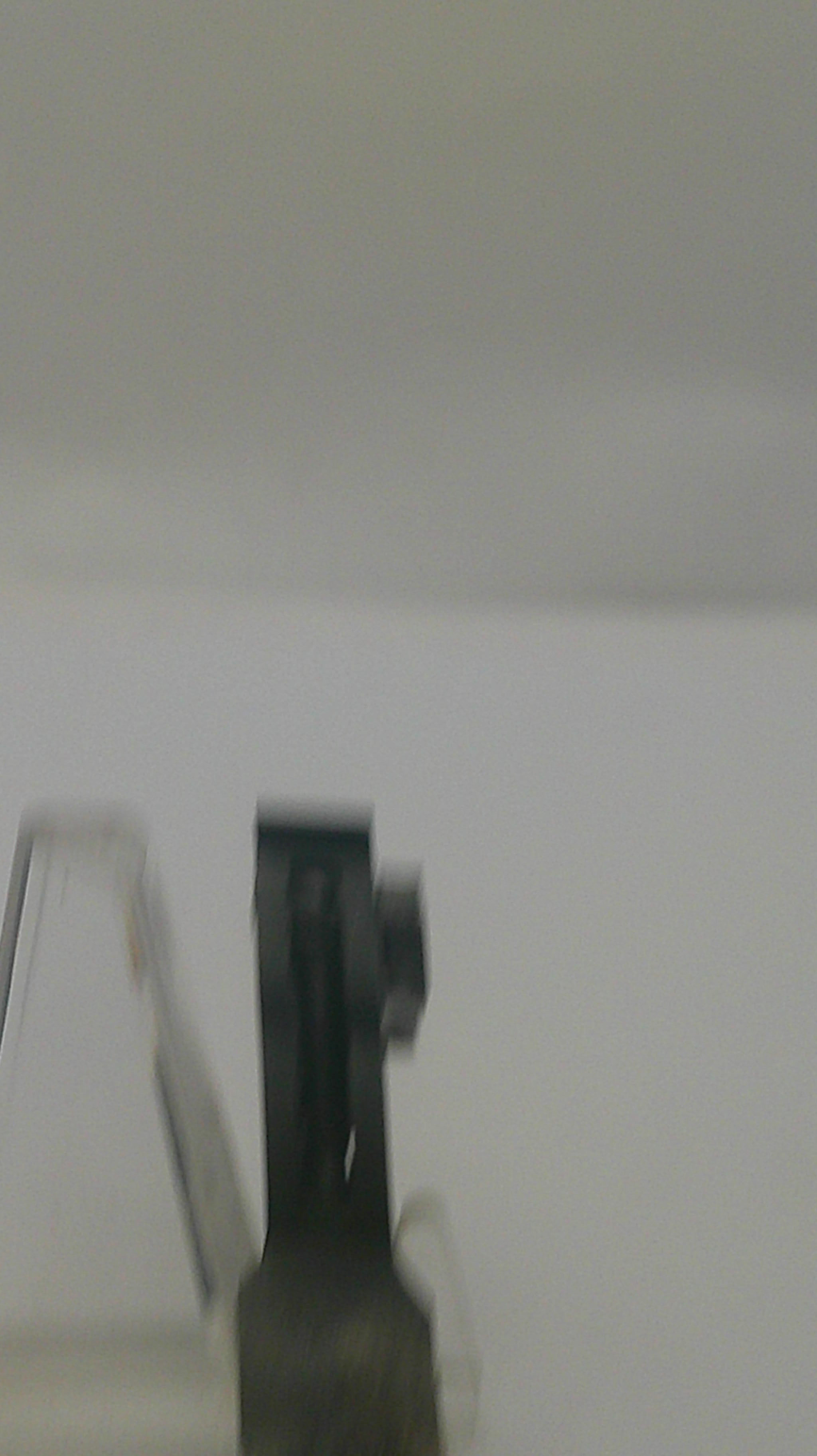 A close-up, slightly blurry shot of a black plastic mounting bracket or clip attached to a light gray or off-white wall.