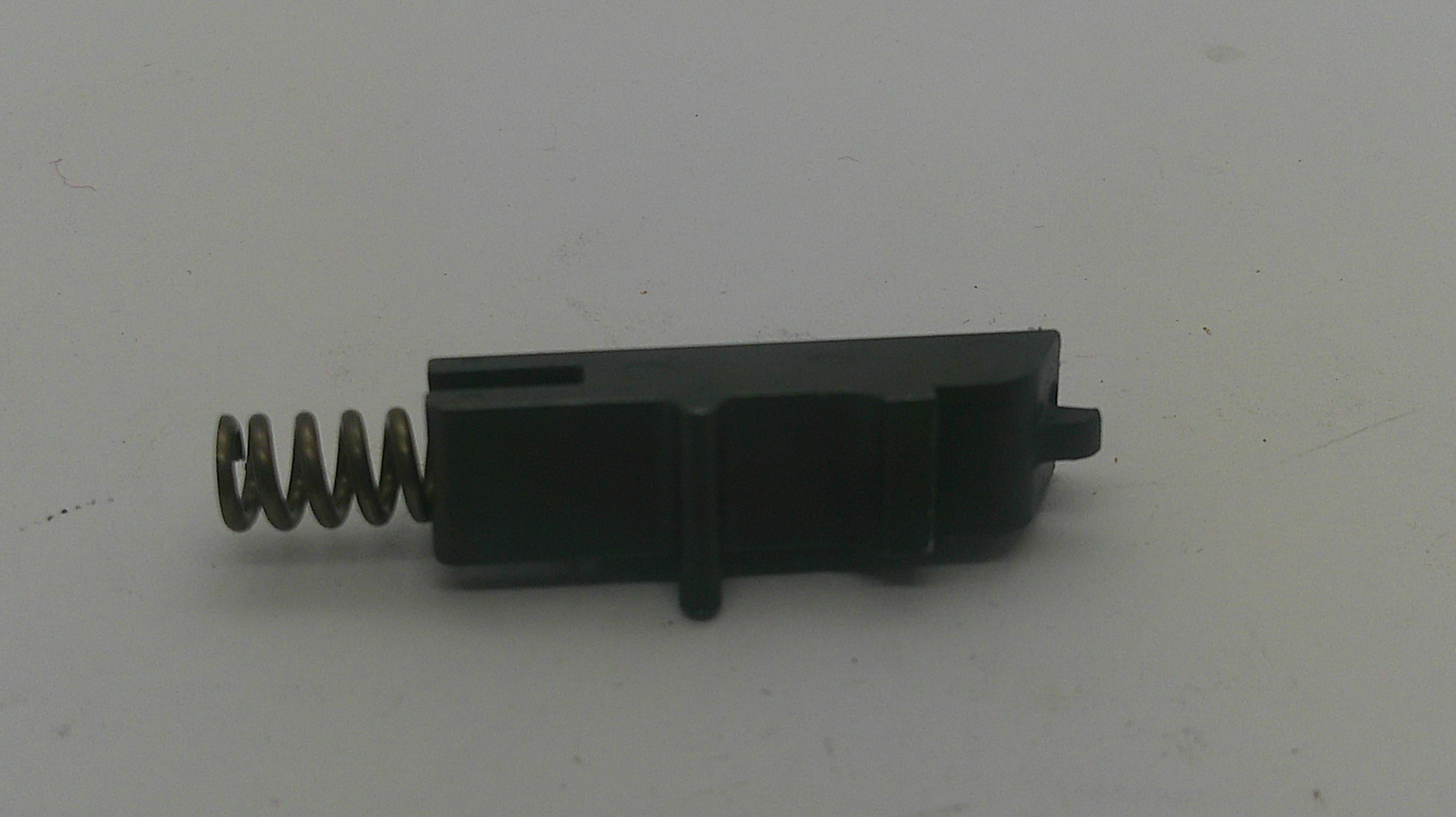 A small black plastic mechanical component with a coiled metal spring attached, photographed on a plain light gray background.