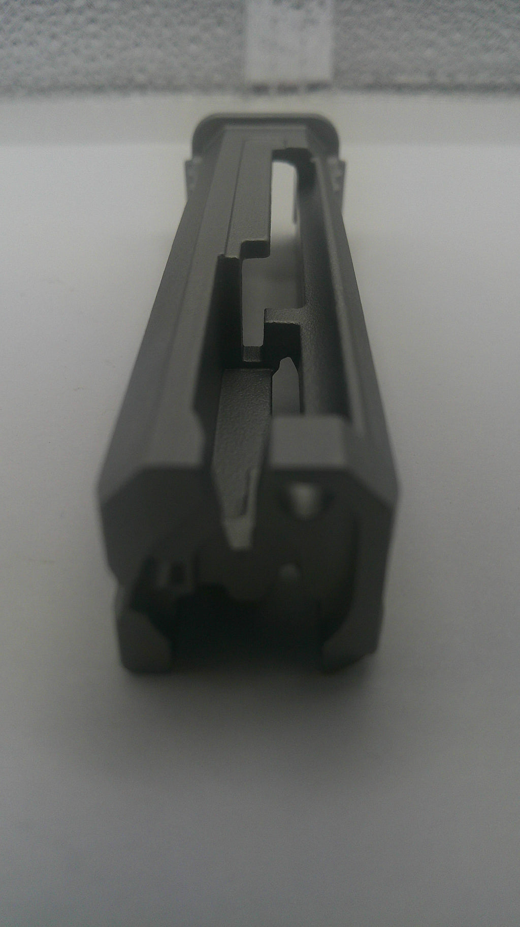 A dark gray plastic replacement part, possibly a handle grip or mechanical component, shown on a plain light gray surface.