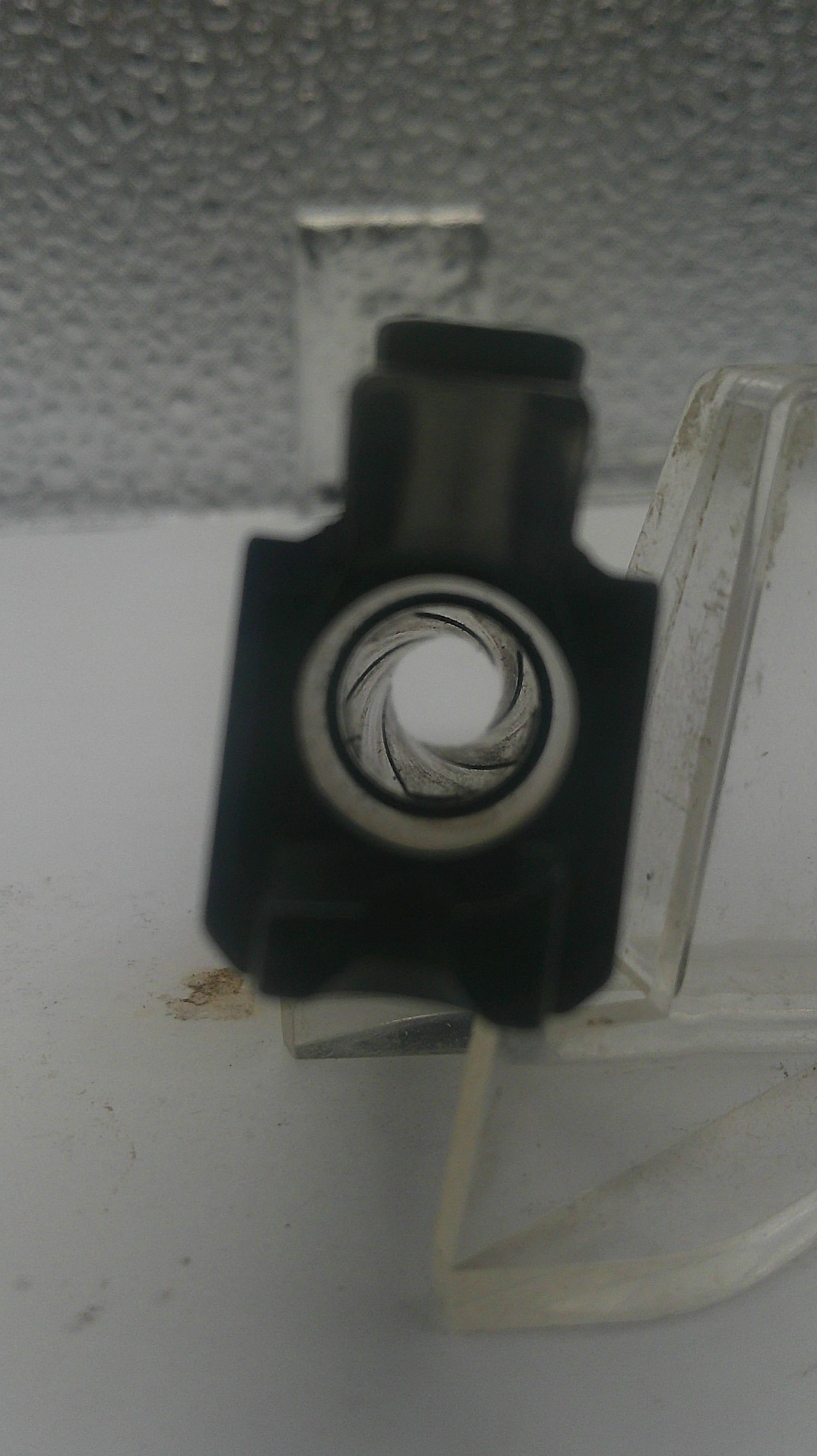 A close-up shot of a black plastic door handle lock cylinder with a clear plastic escutcheon, mounted on a white textured surface.