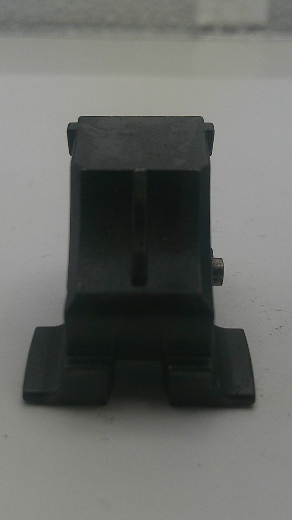 A black plastic mounting bracket or clip with a small silver screw visible at the bottom center, photographed against a plain light gray background.