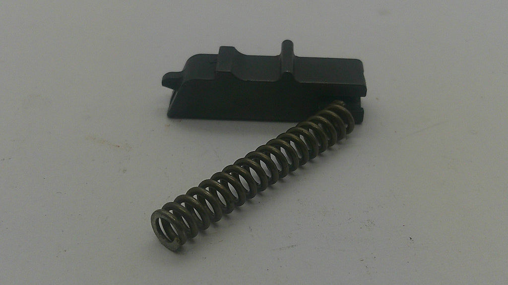 A black plastic trigger component with a coiled metal spring, photographed on a plain light gray surface.