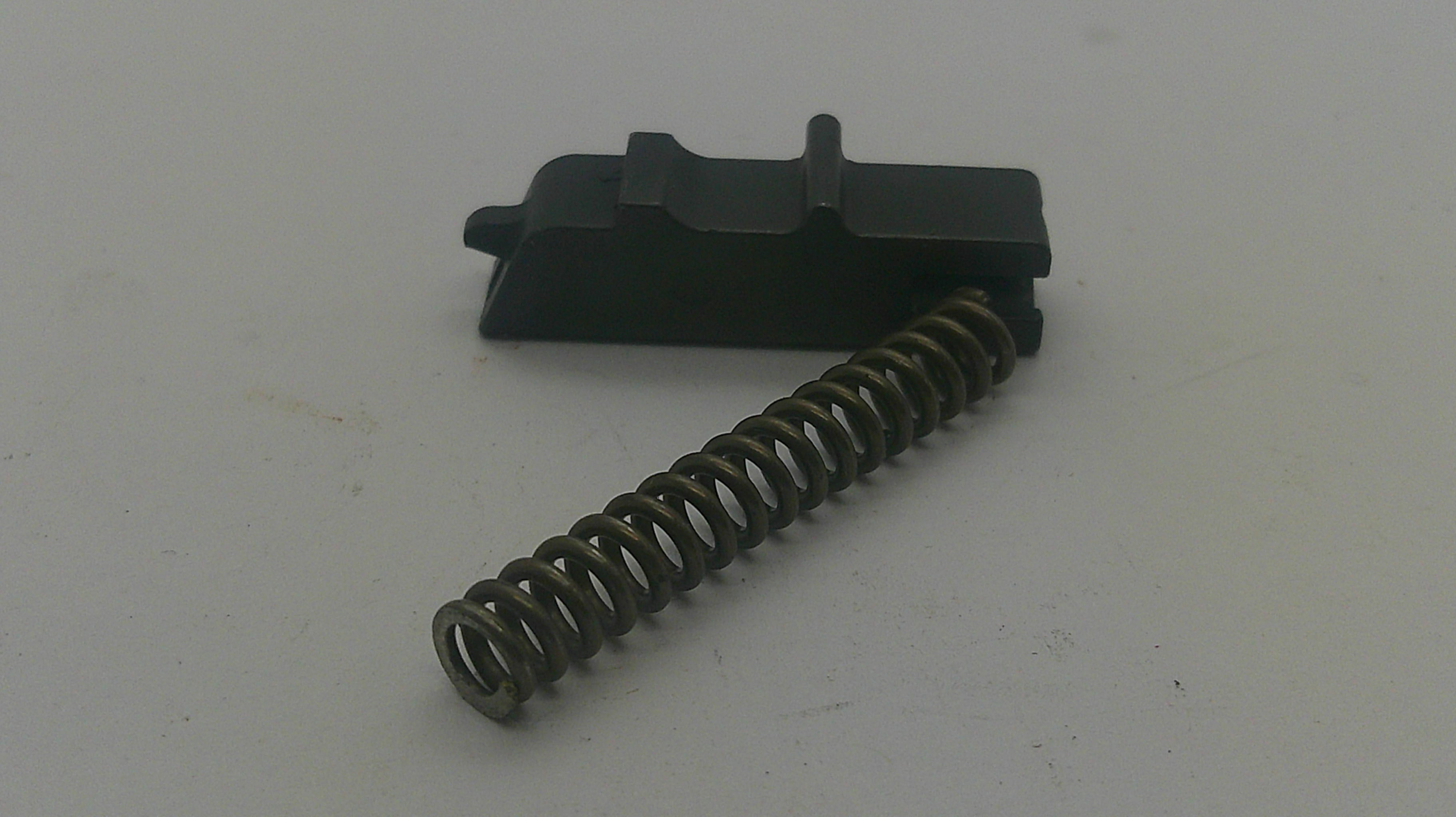 A black plastic trigger component with a coiled metal spring, photographed on a plain light gray surface.