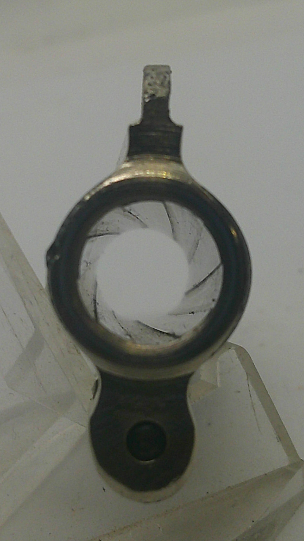 A close-up of a circular metal component with a dark rim, a central hole, and a small protruding tab, photographed against a light gray background.