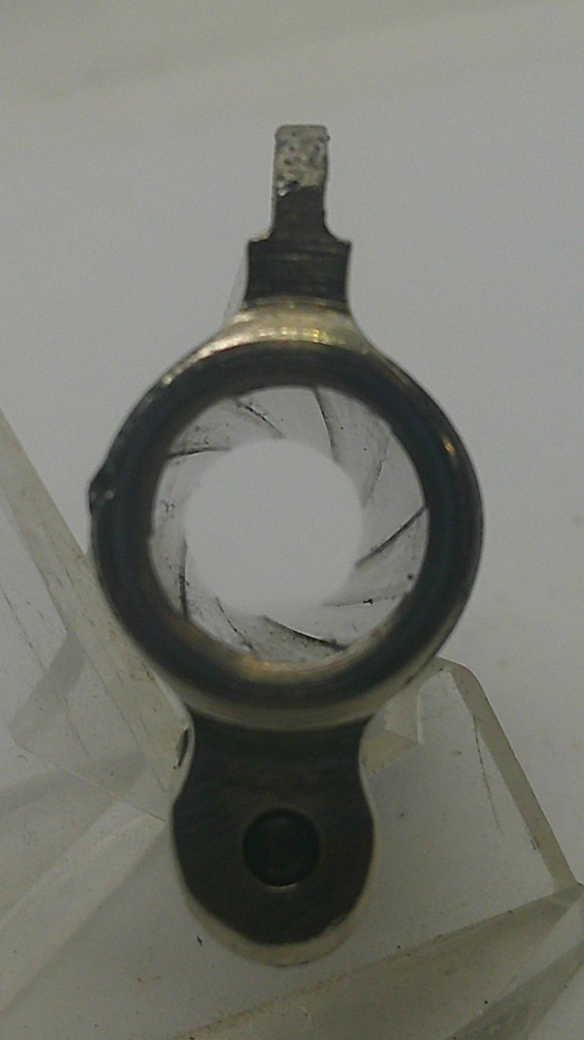 A close-up of a circular metal component with a dark rim, a central hole, and a small protruding tab, photographed against a light gray background.