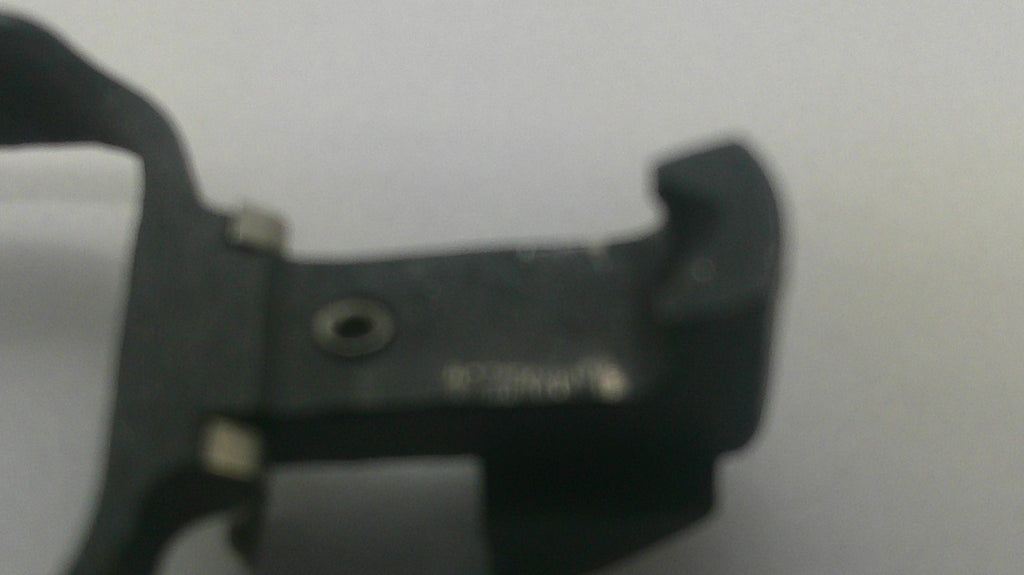 A close-up of a black plastic or metal mechanical component with a small circular hole and faint stamped markings, photographed against a plain light background.