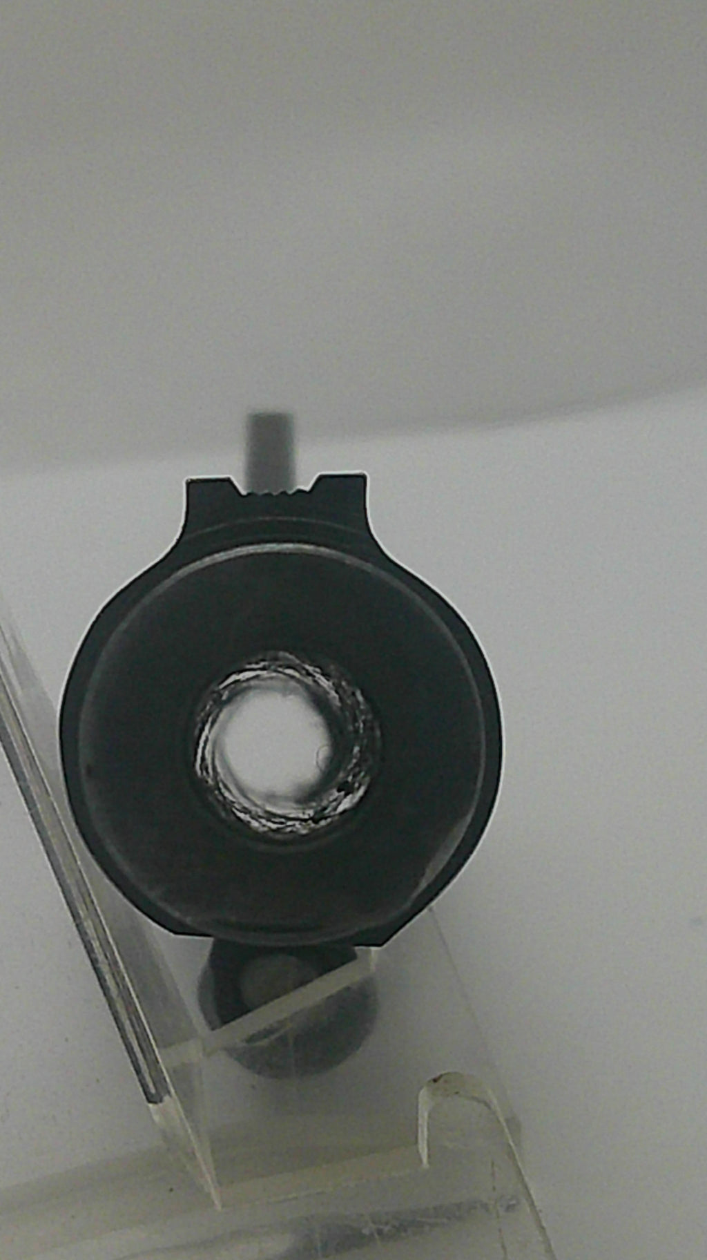 A close-up of a black circular component with a central hole, mounted on a clear plastic frame against a plain light background.