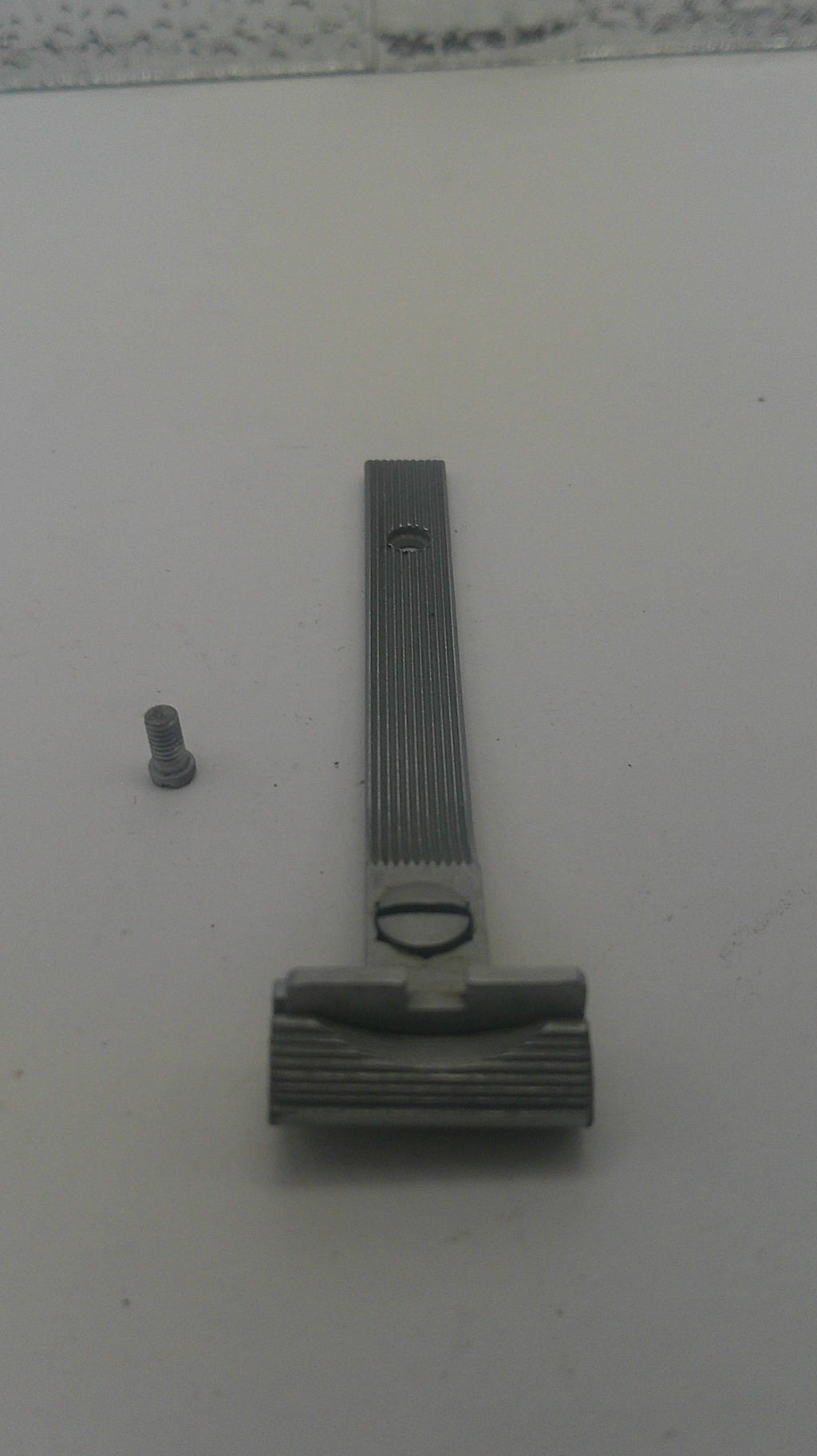 A gray metal door stopper with a ribbed handle and a small gray screw, shown on a plain off-white surface.