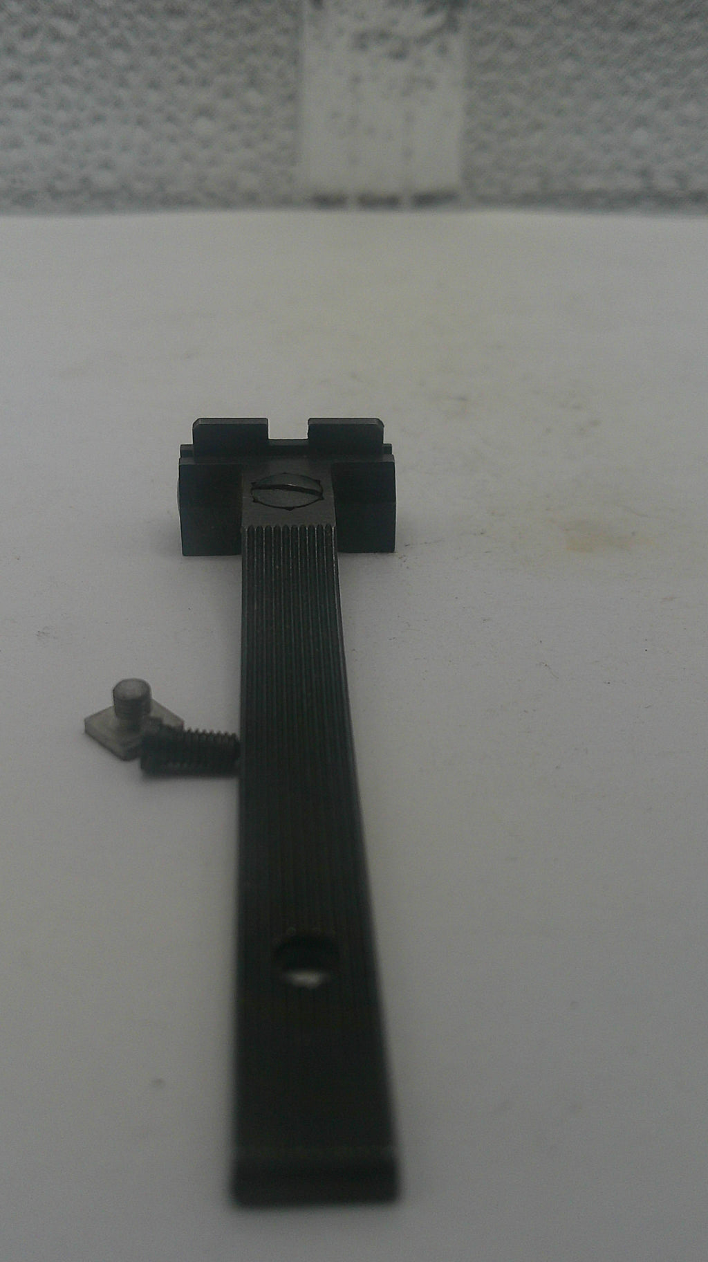 A black metal latch or bracket with a screw fastener, shown mounted against a plain off-white surface.