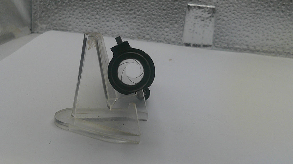 Small black and green object on a clear stand against a white background