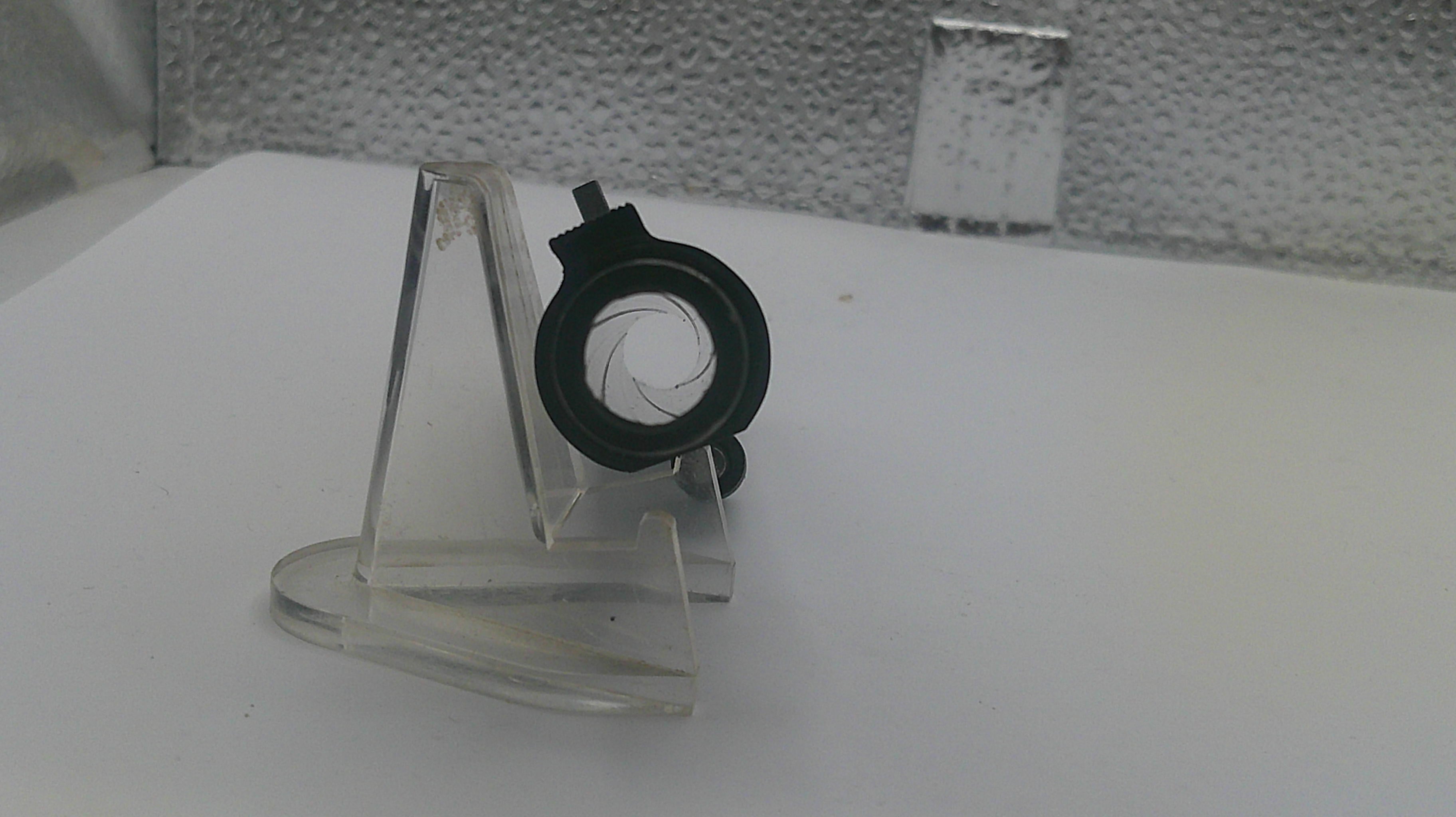 Small black and green object on a clear stand against a white background