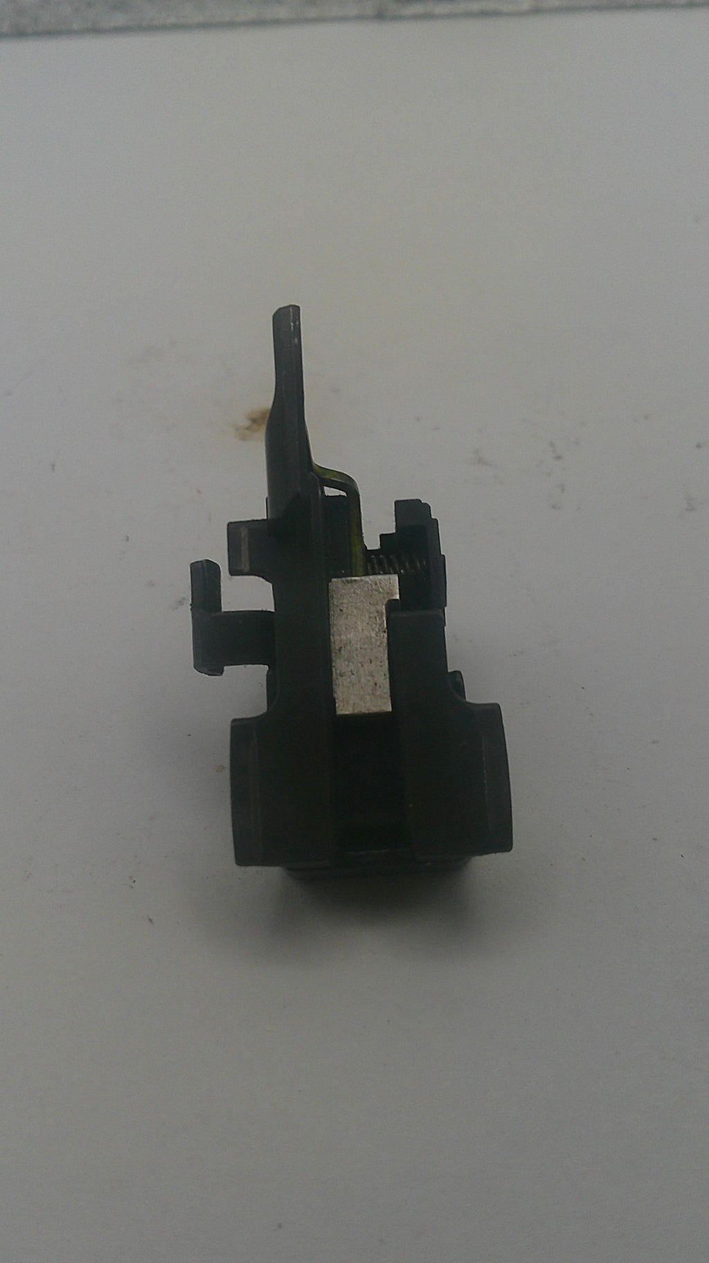 A small black plastic mechanical component, likely a lock pick or key cylinder part, resting on a plain off-white surface.