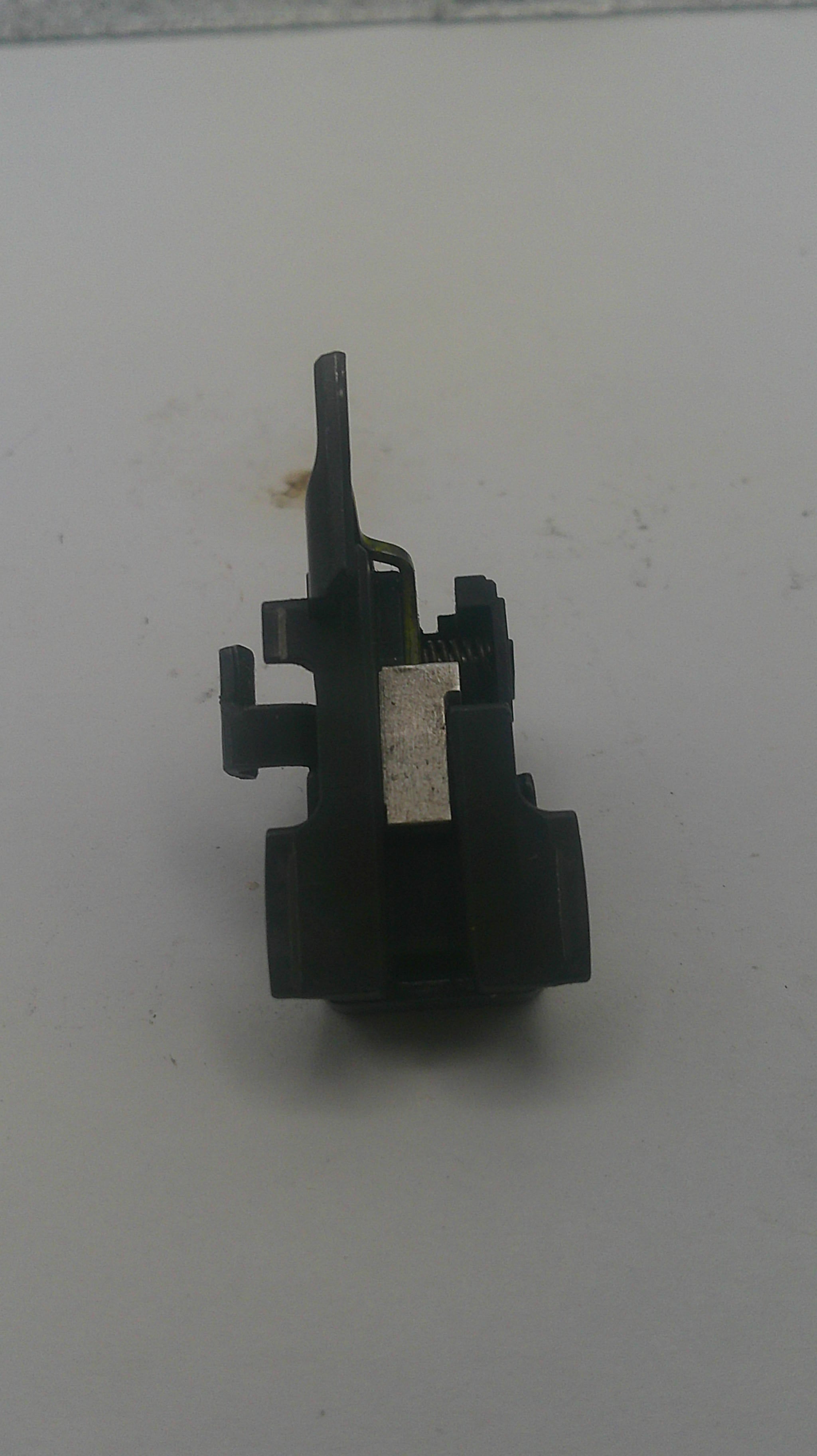 A small black plastic mechanical component, likely a lock pick or key cylinder part, resting on a plain off-white surface.