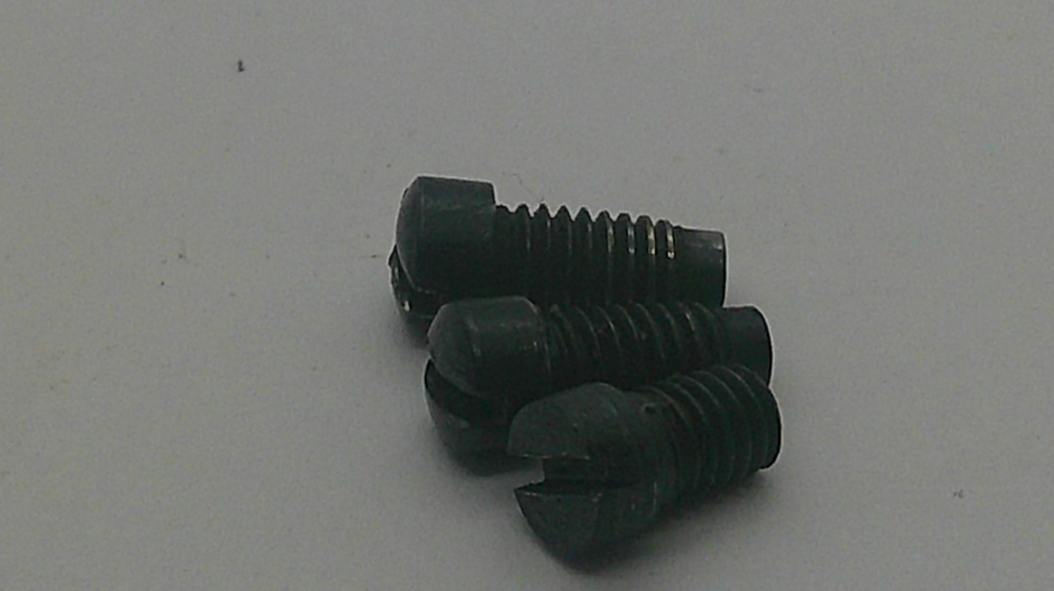 Three small black plastic slotted screws with threaded bodies, arranged on a plain light gray surface.