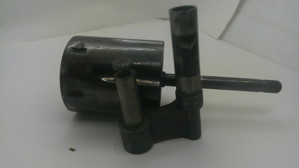 A used dark metal mechanical part, possibly a bearing, pulley, or guide assembly, featuring a cylindrical housing, vertical shafts, and a horizontal rod, photographed on a plain white surface.