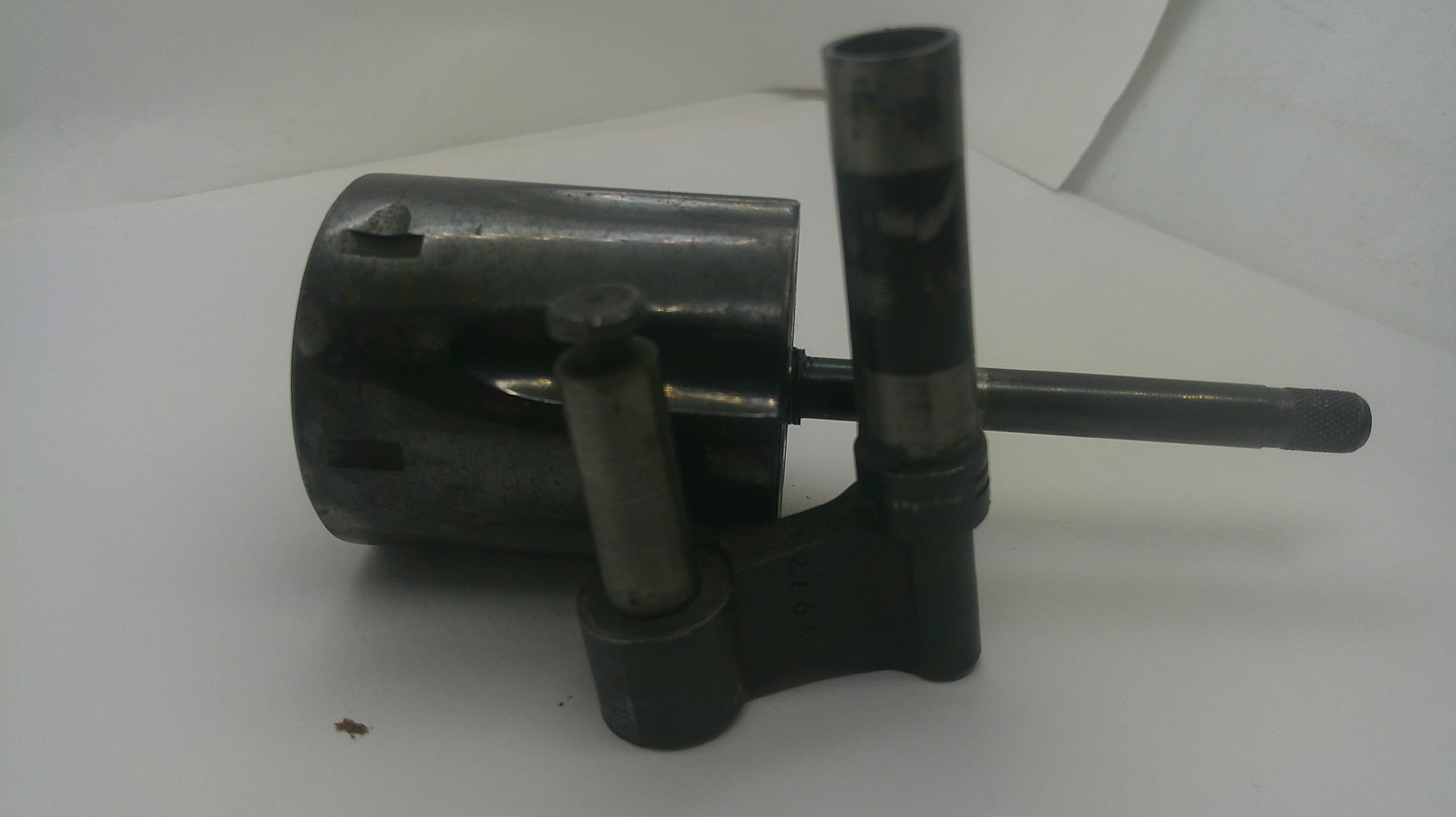 A used dark metal mechanical part, possibly a bearing, pulley, or guide assembly, featuring a cylindrical housing, vertical shafts, and a horizontal rod, photographed on a plain white surface.