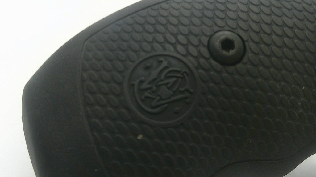 Close-up of a black textured grip with a circular embossed logo and a small screw detail, photographed against a white background.