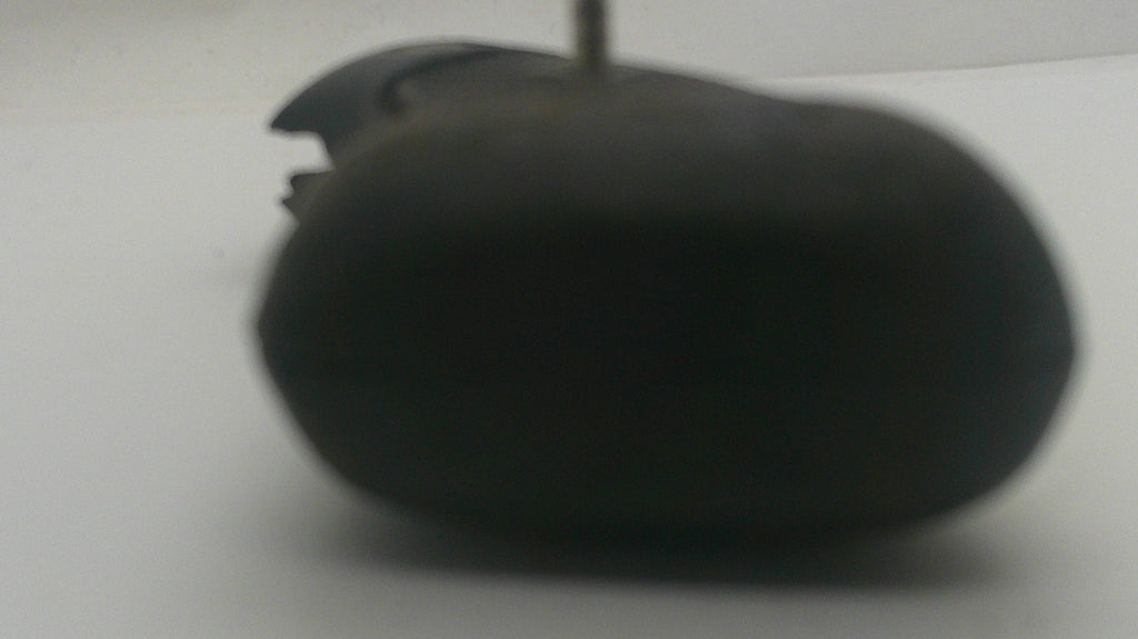 A close-up, low-resolution shot of a black, oval-shaped object, possibly a mouse pad or a small accessory, on a plain white surface.