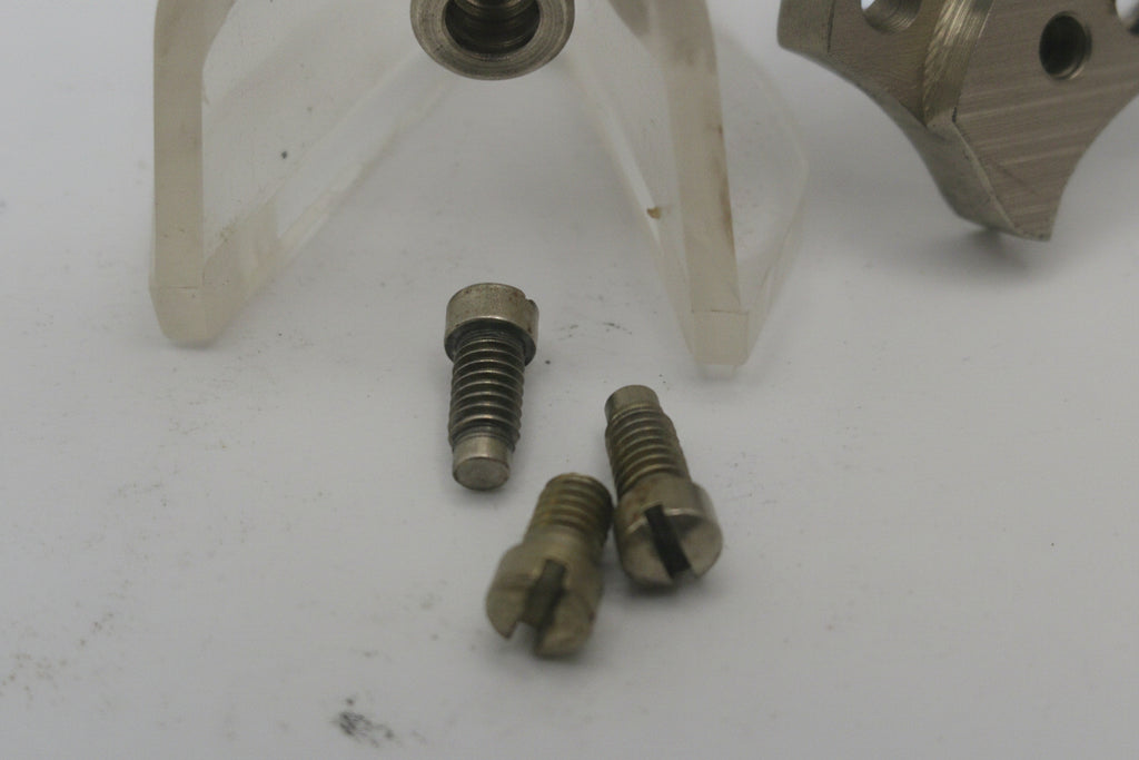 Three metal screws on a white surface with a blurred tool in the background