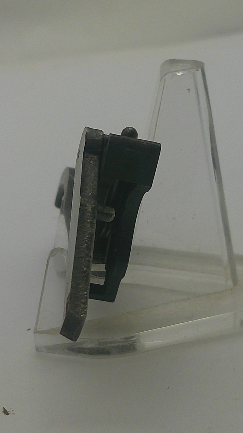A close-up of a black plastic hook with a clear plastic mounting bracket attached to a plain white wall.