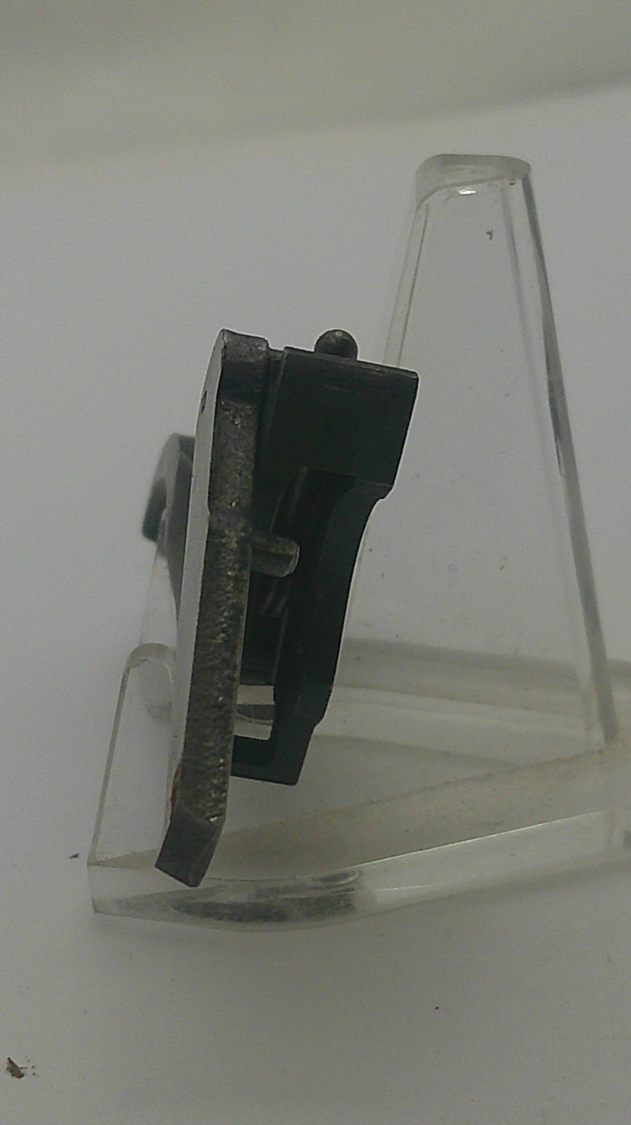 A close-up of a black plastic hook with a clear plastic mounting bracket attached to a plain white wall.