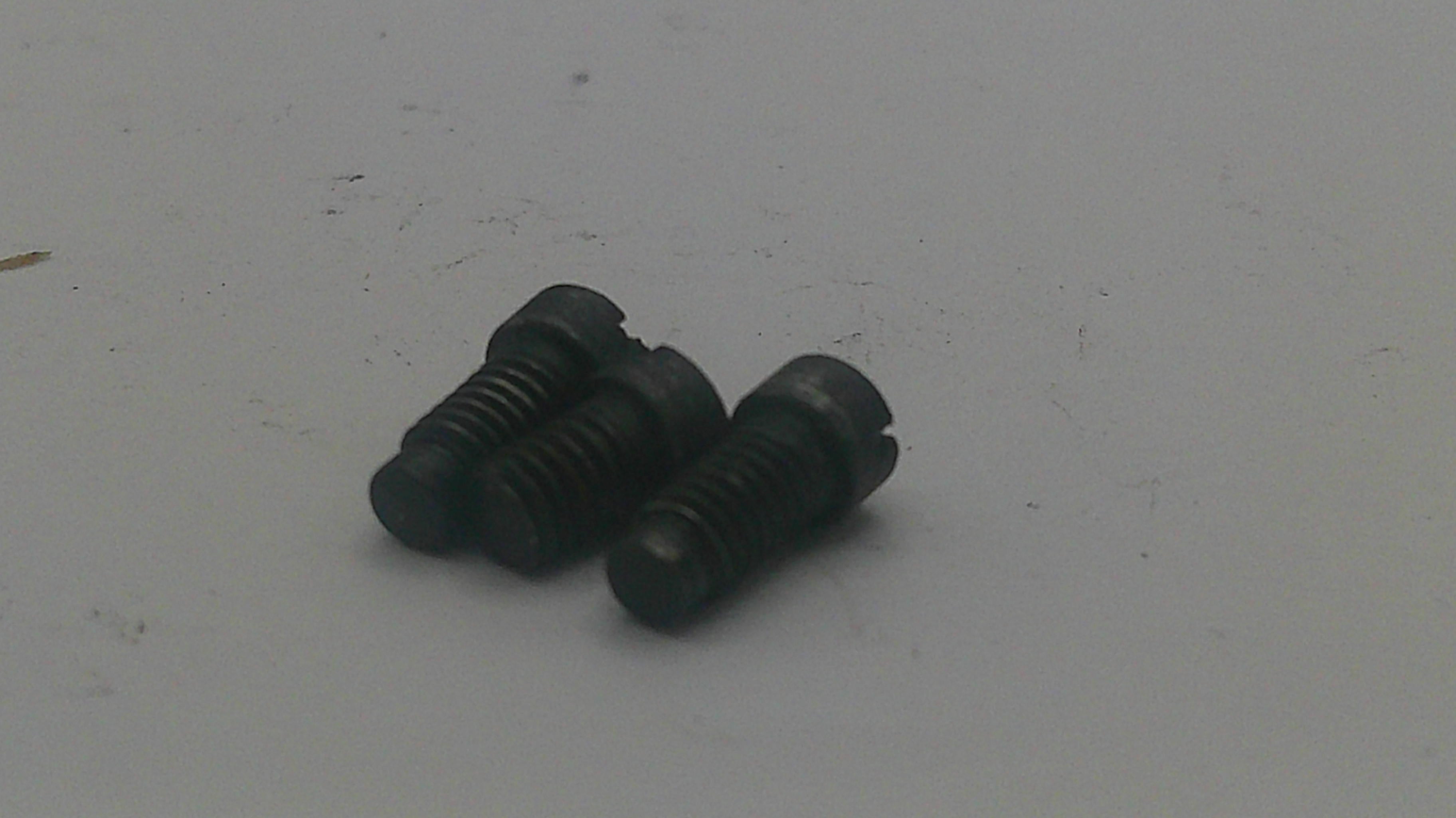 Three small black metal slotted screws on a plain light gray surface.