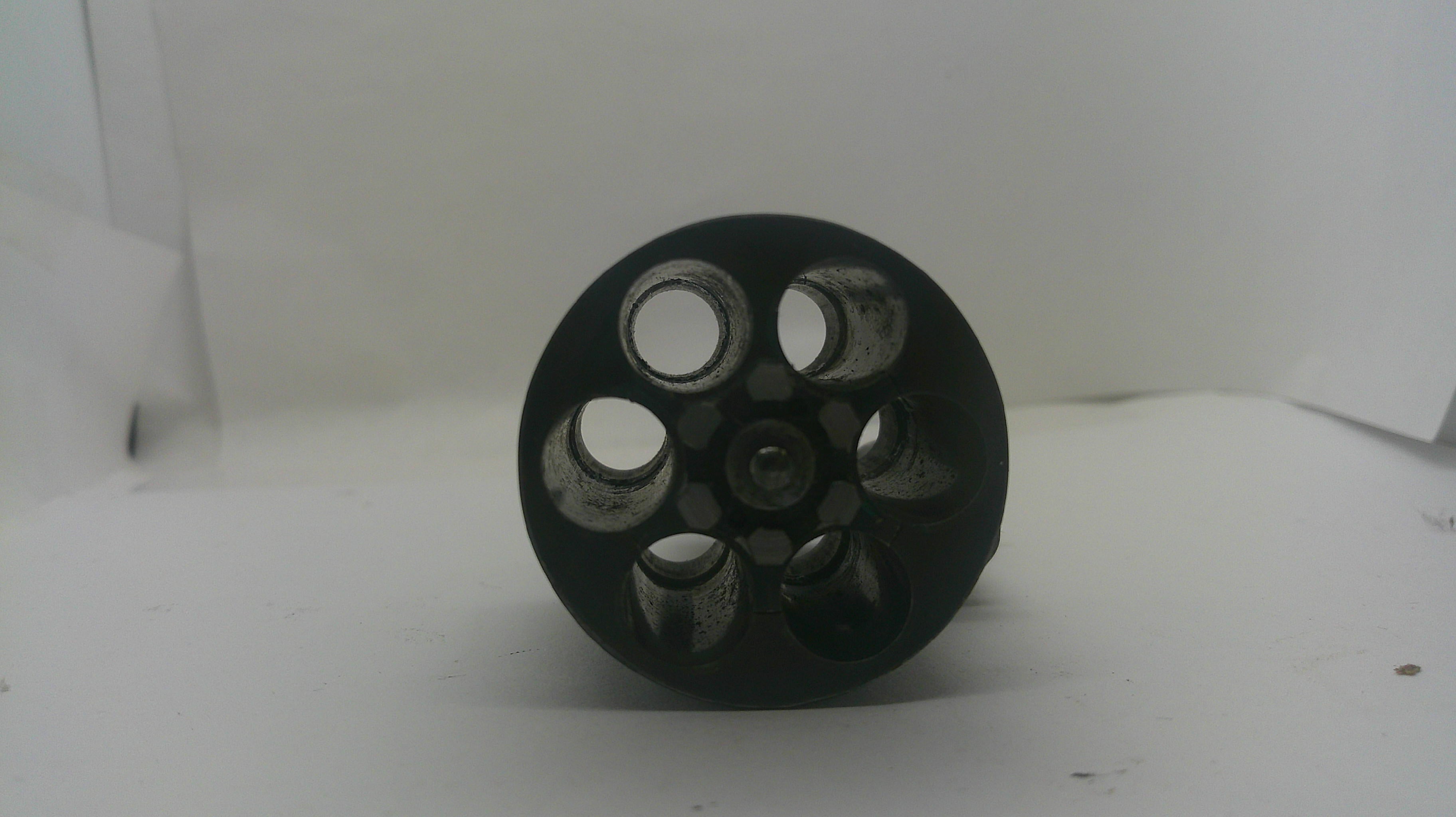 A black circular wheel or pulley with six circular cutouts, photographed on a plain white background.