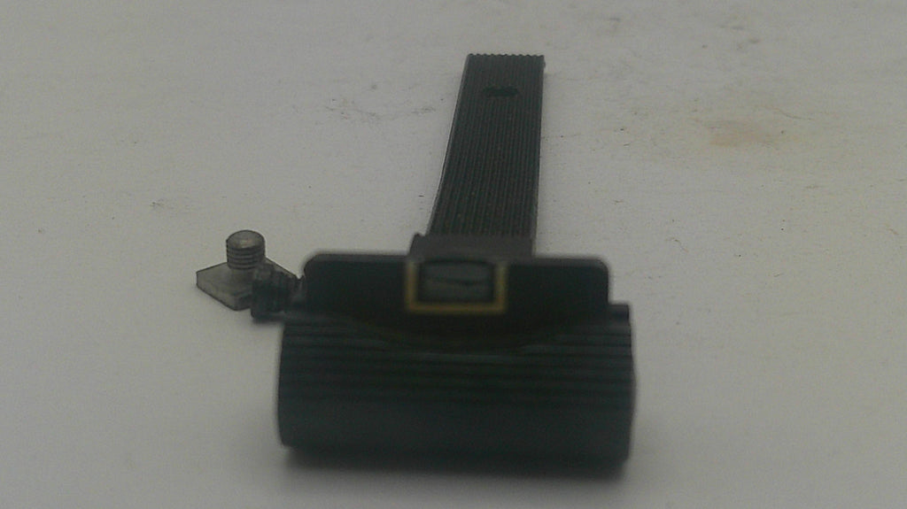 A close-up of a black textured plastic component with a small gold accent and a separate small metal screw piece, photographed on a plain light surface.