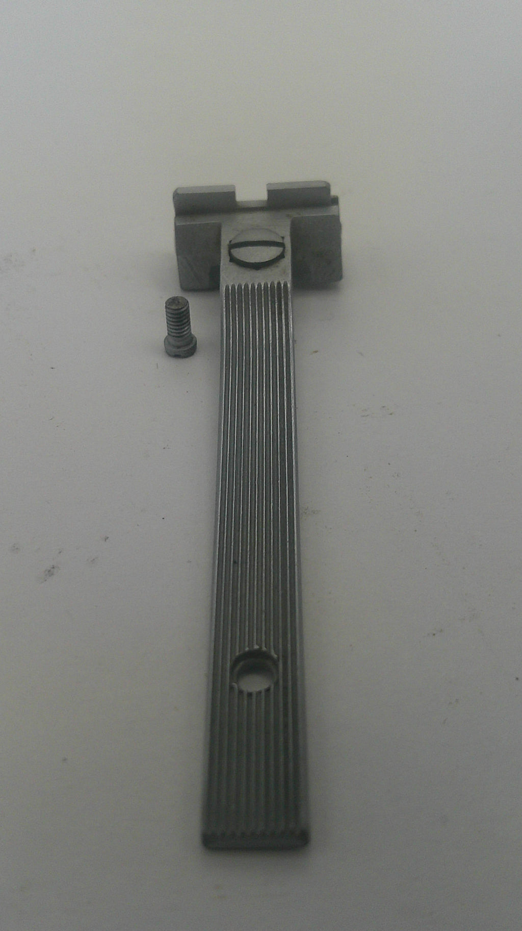 A small metal latch or bracket component with a ribbed rectangular bar, a screw, and a mounting piece, photographed on a plain light background.