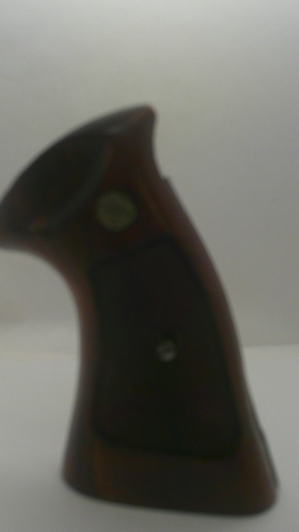 A close-up of a dark brown wooden object with a black grip panel and a small round metallic detail, photographed against a plain light background.