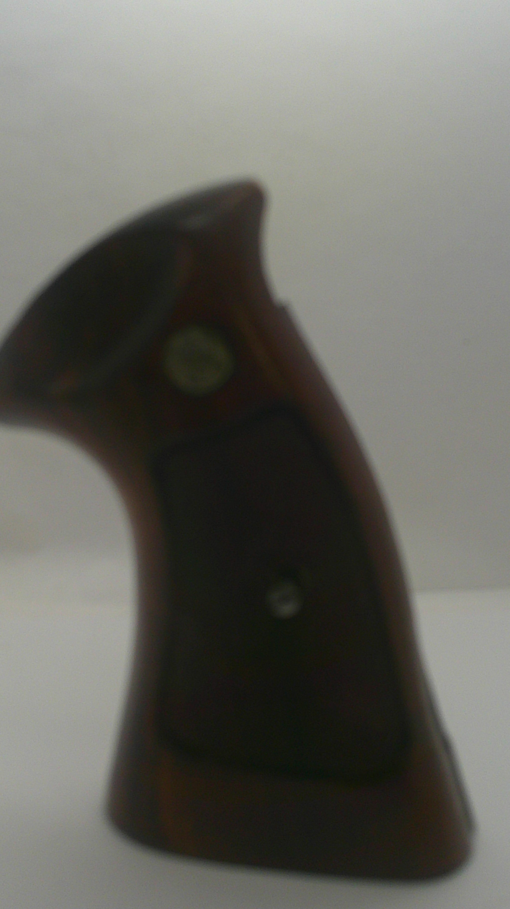 A close-up of a dark brown wooden object with a black grip panel and a small round metallic detail, photographed against a plain light background.