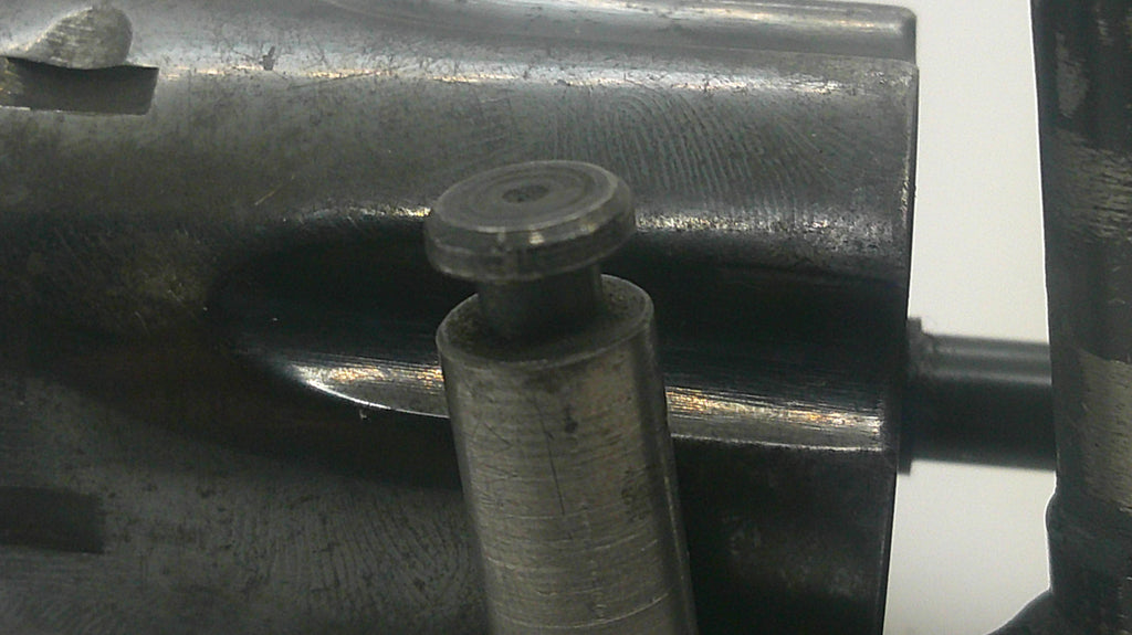 A close-up view of a dark metallic mechanical component with a cylindrical pin or bolt protruding from a machined metal housing.
