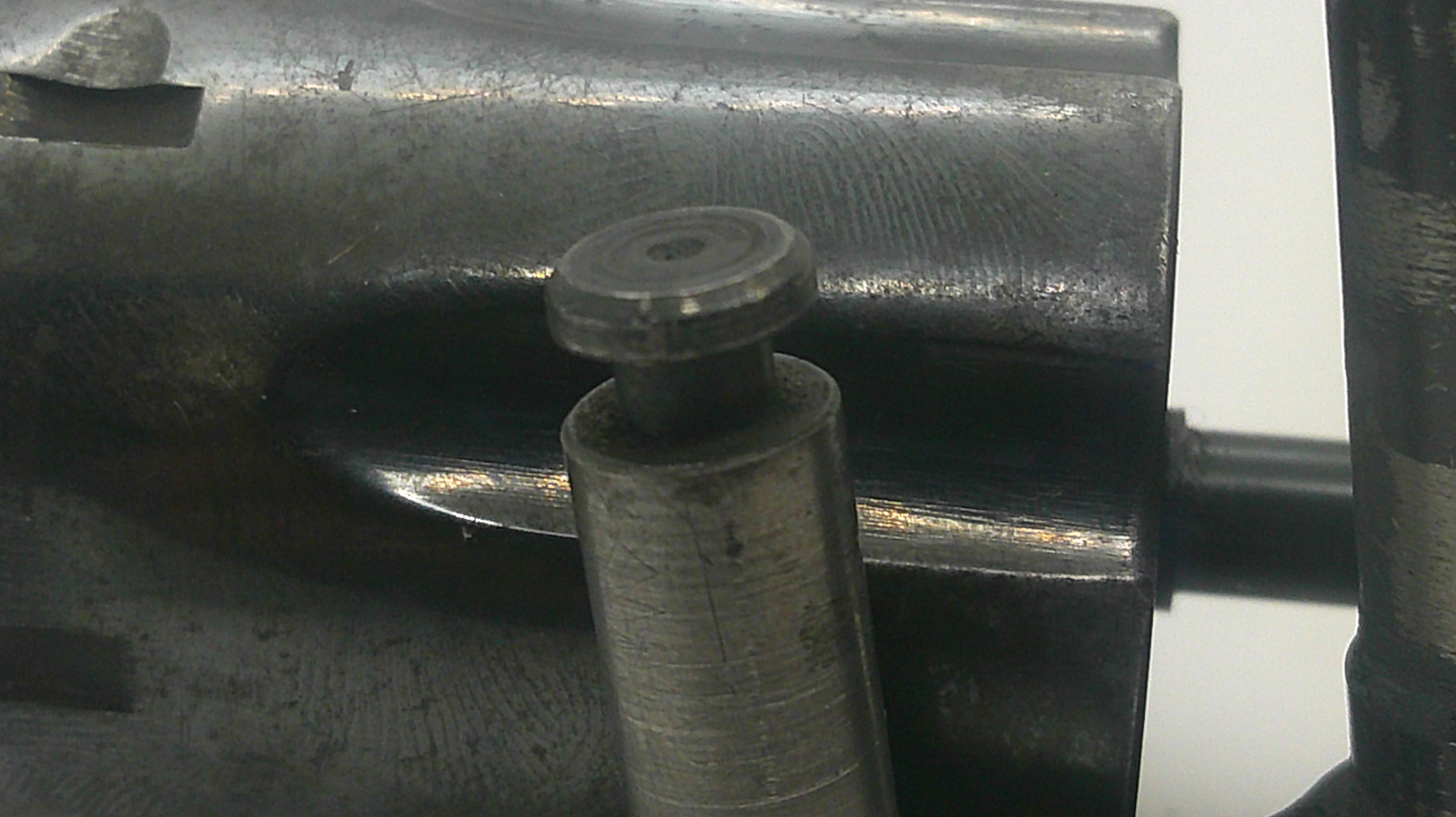 A close-up view of a dark metallic mechanical component with a cylindrical pin or bolt protruding from a machined metal housing.