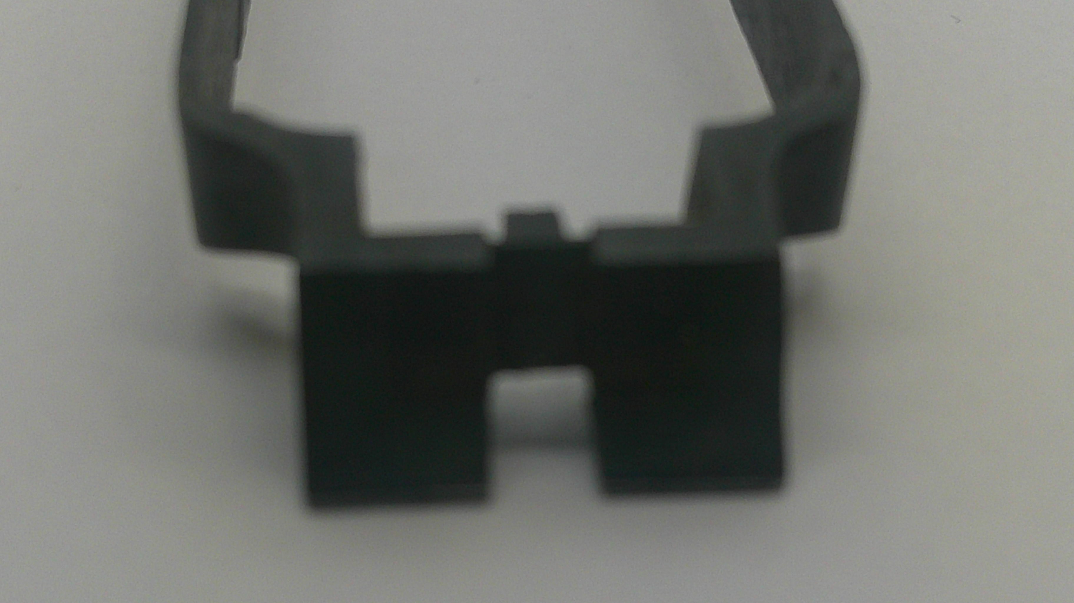 A close-up of a small black plastic or rubber clip-like component on a plain light background.