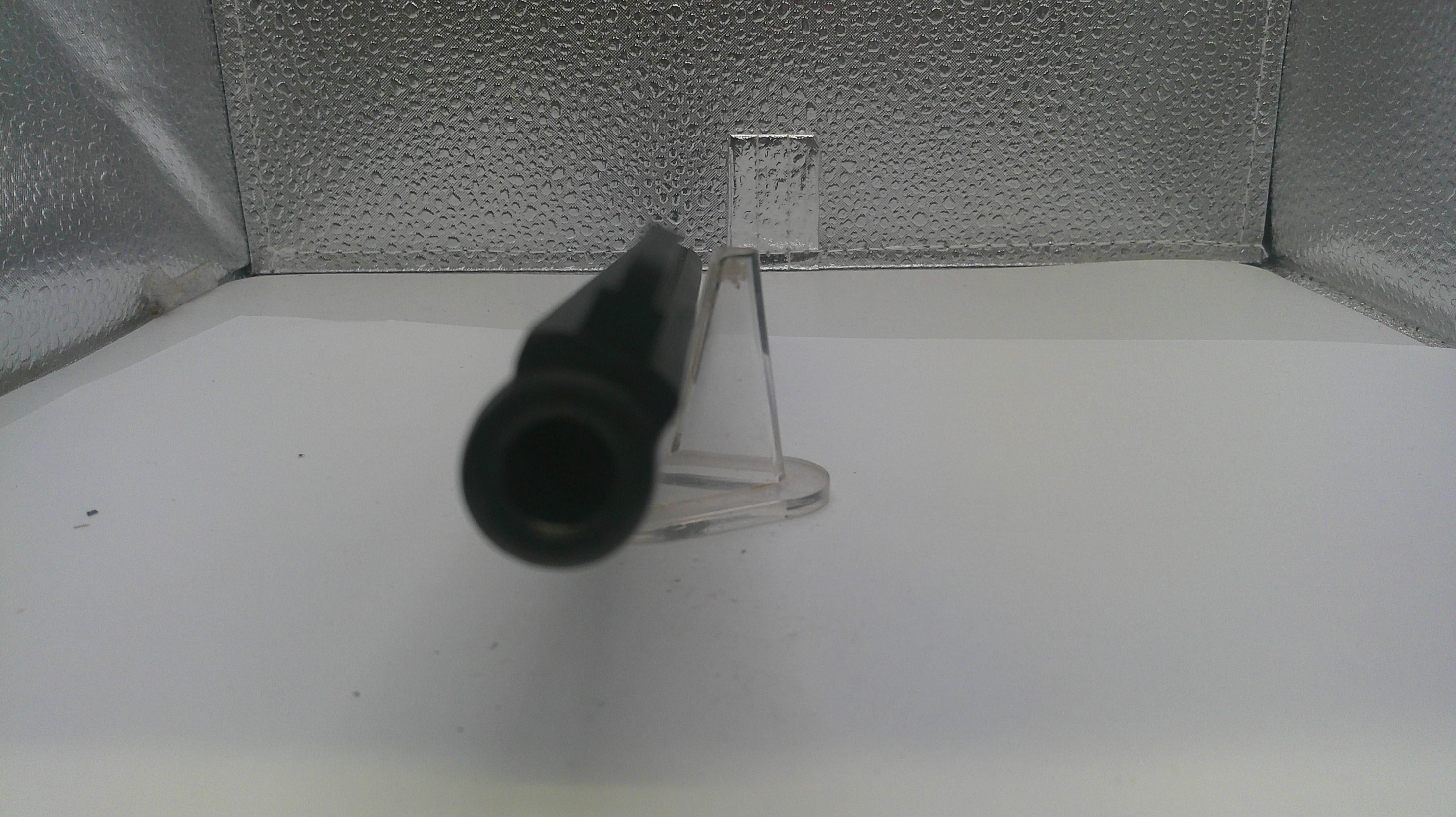 A close-up of a black cylindrical object, possibly a tool or accessory, resting on a clear plastic stand against a textured silver background.