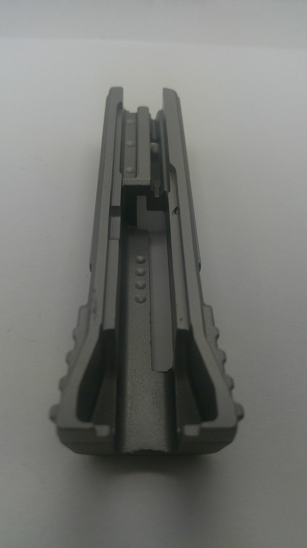 A gray plastic or metal clip-like component with a textured outer edge and internal slots, photographed on a plain light background.