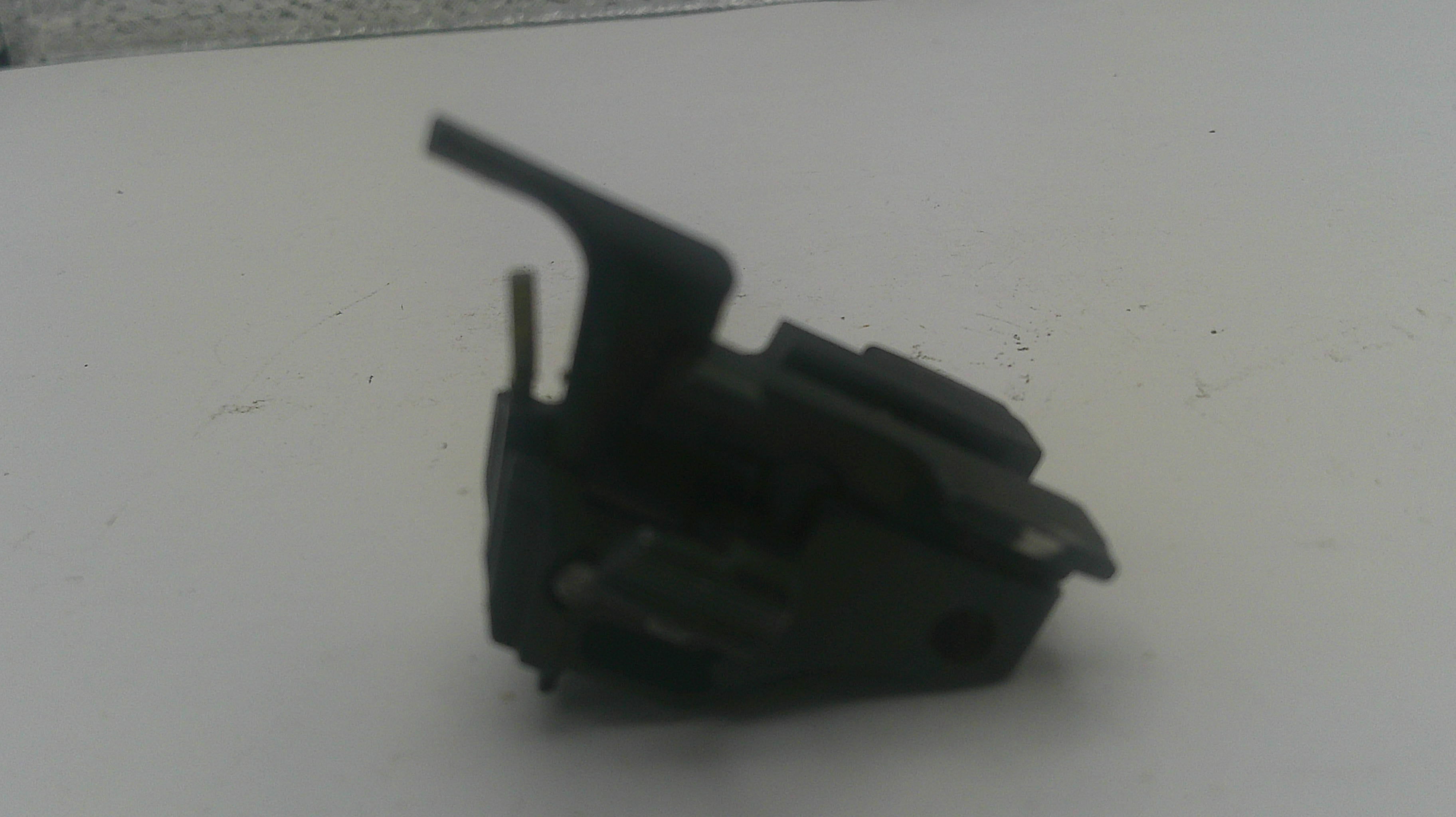 A small black plastic mechanical component or switch with a lever, photographed on a plain light surface.