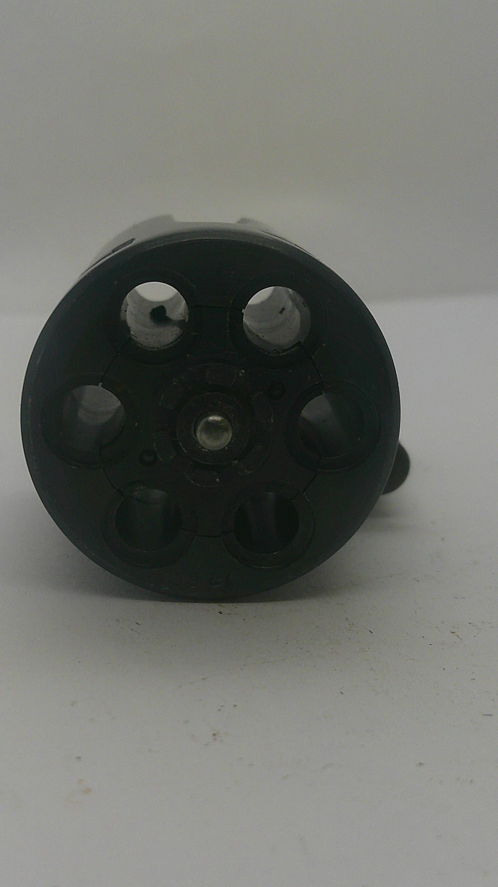 A black plastic six-hole revolver magazine or shell holder, photographed from an angled top-down view against a plain off-white background.