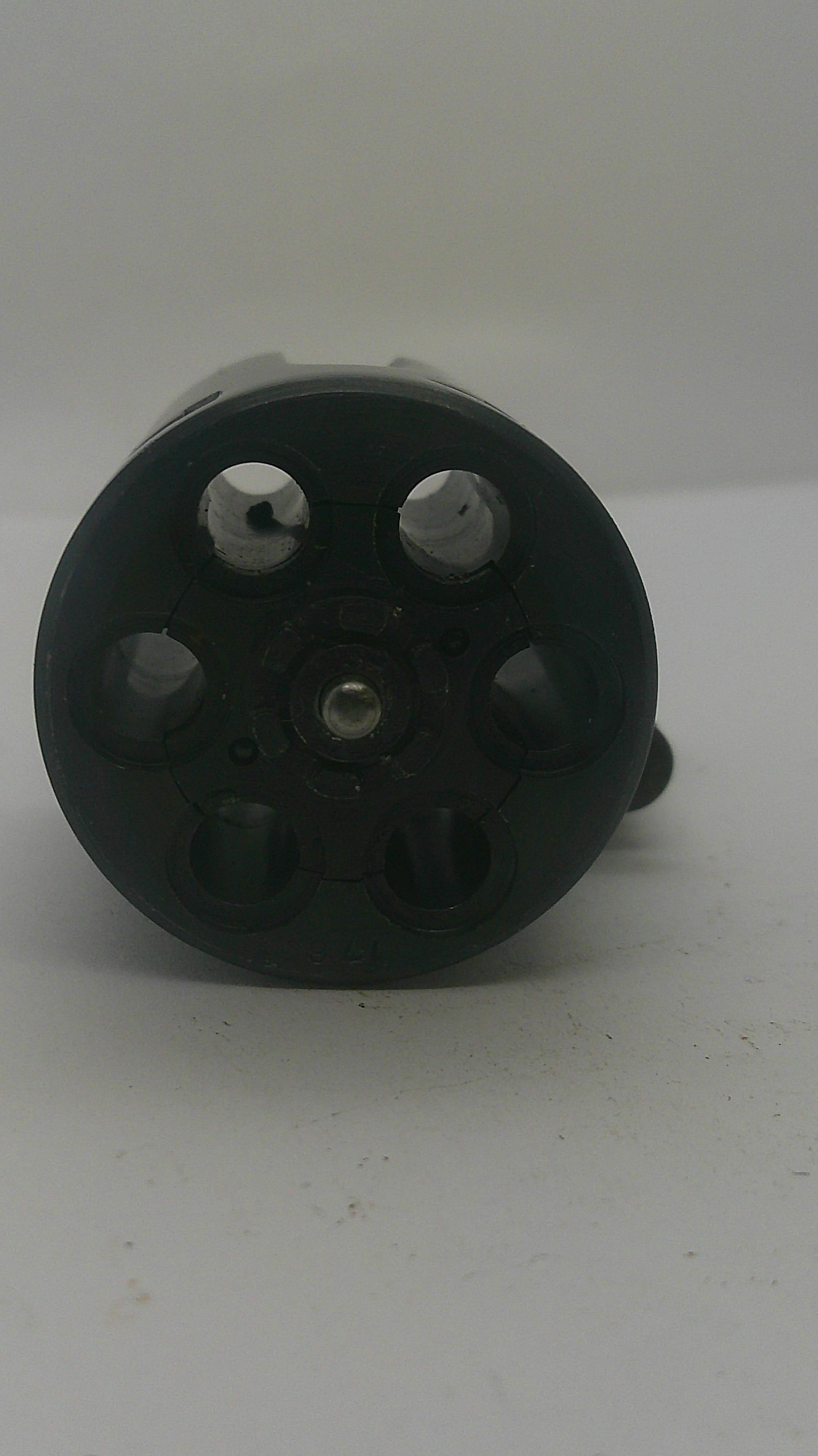 A black plastic six-hole revolver magazine or shell holder, photographed from an angled top-down view against a plain off-white background.